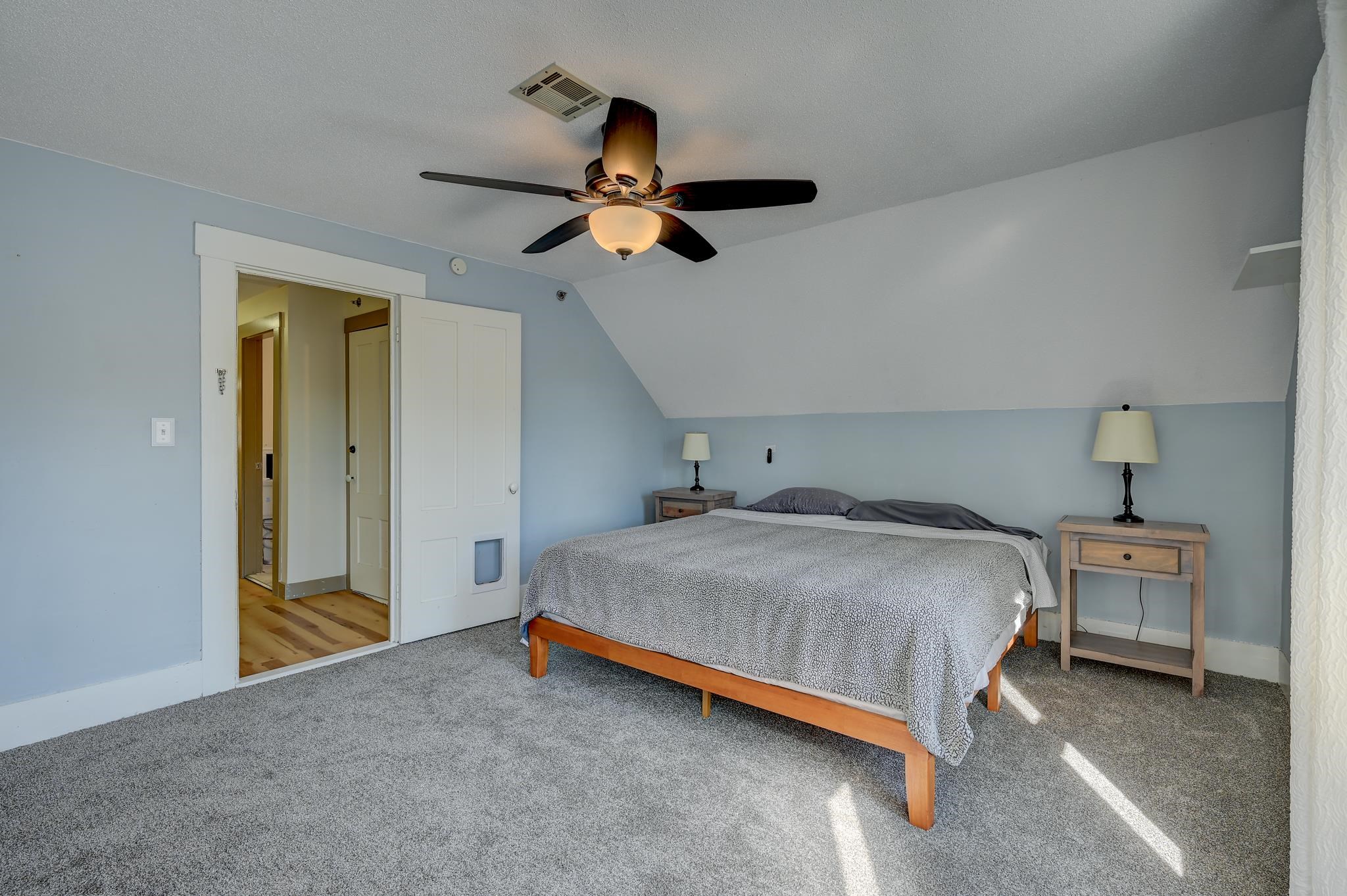 Bedroom with a wooden bed, pale blue walls, sloped ceiling, and ceiling fan.