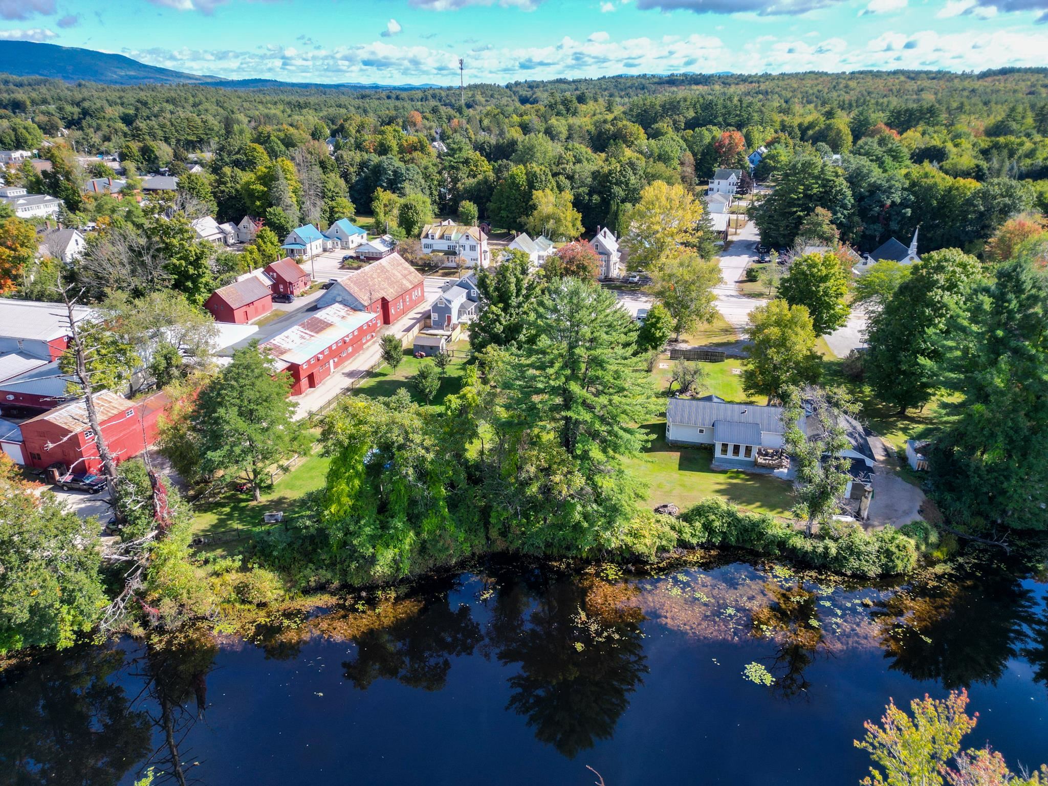 Aerial view of a riverside Conway neighborhood with red barns and wooded mountains in the distance.