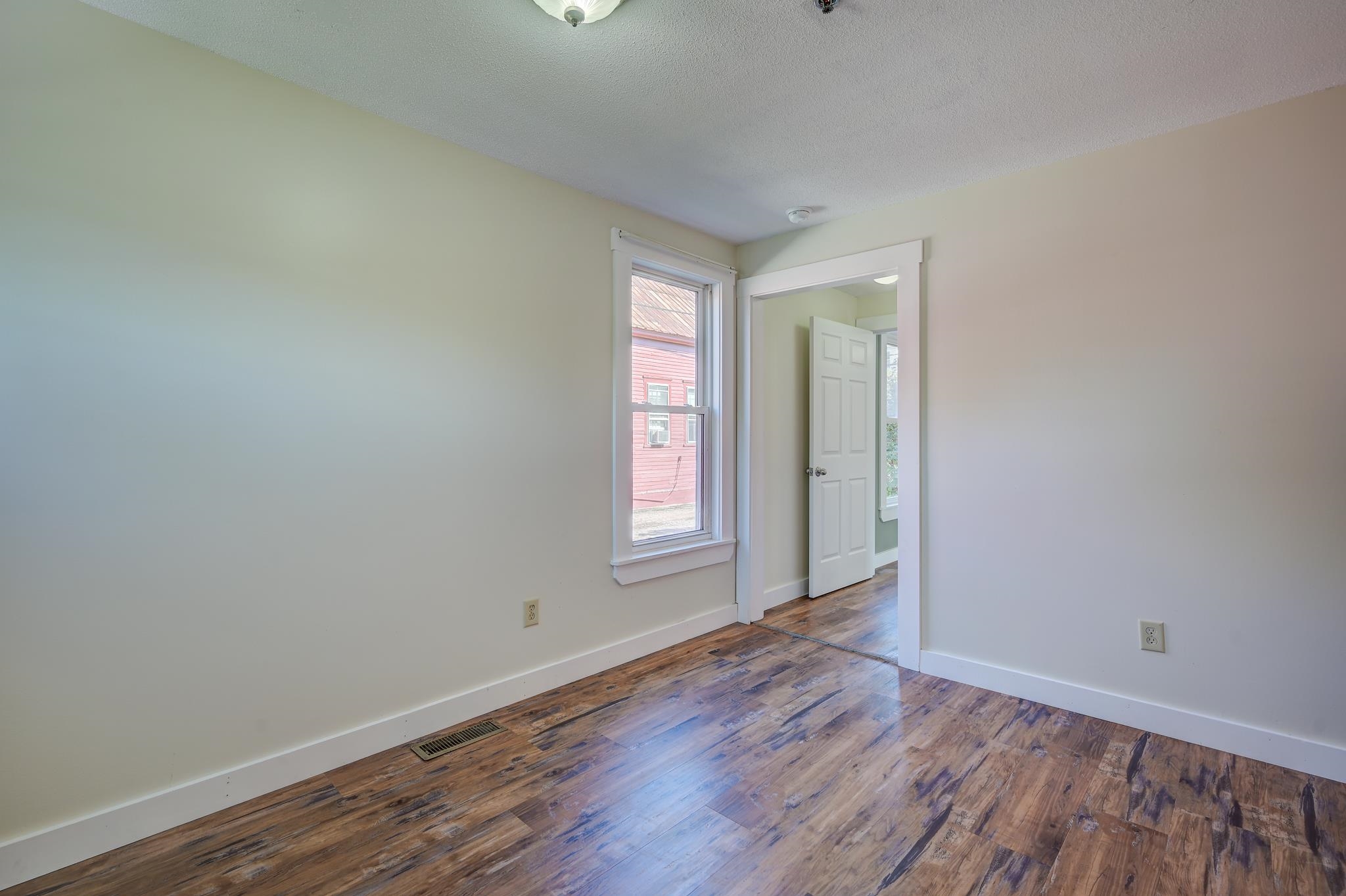 Empty room with wood-look plank flooring, a tall window, and an open doorway.