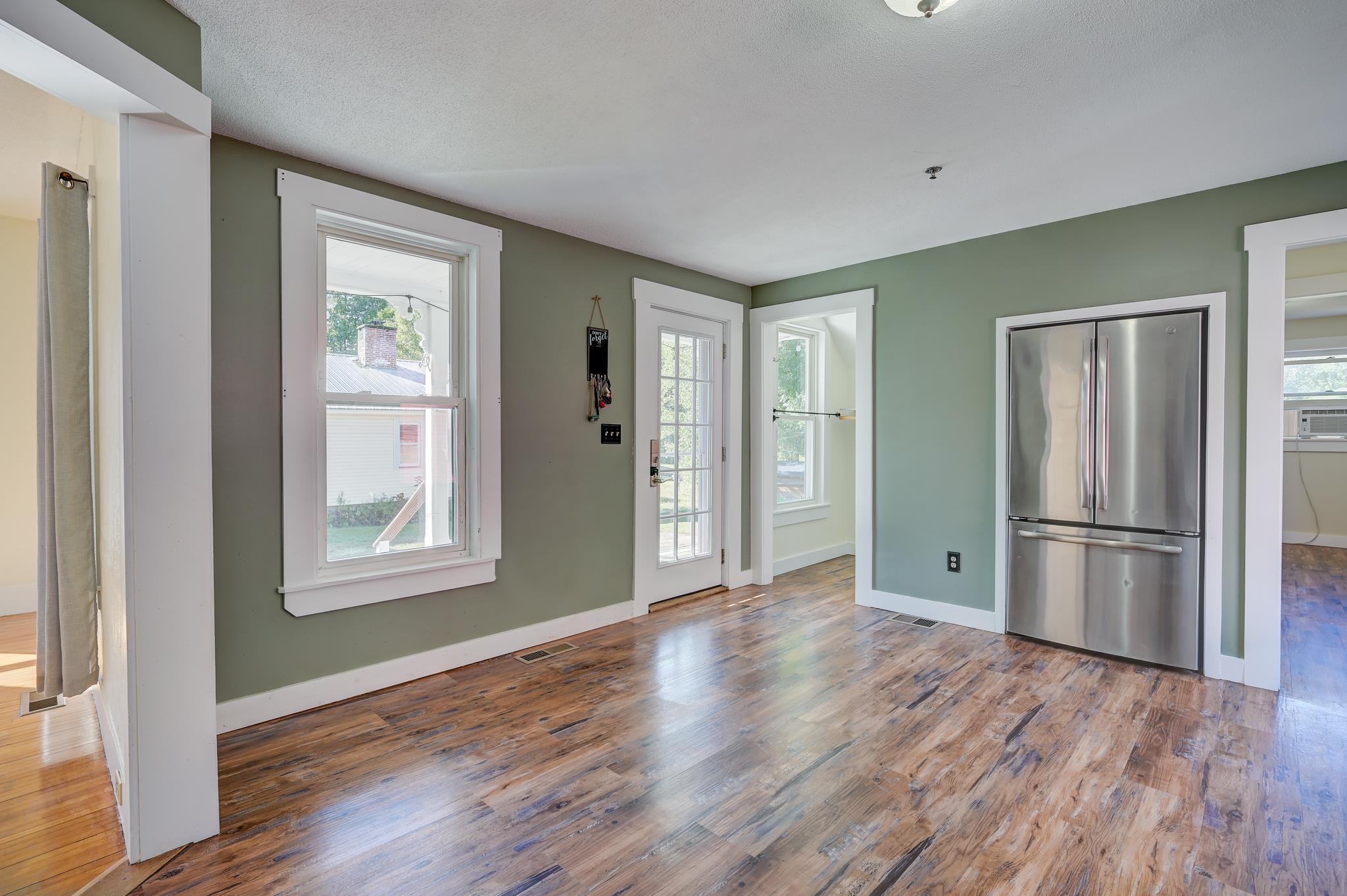 Kitchen with sage-green walls, wood-look floors, a stainless steel refrigerator, and a glass-paneled door.