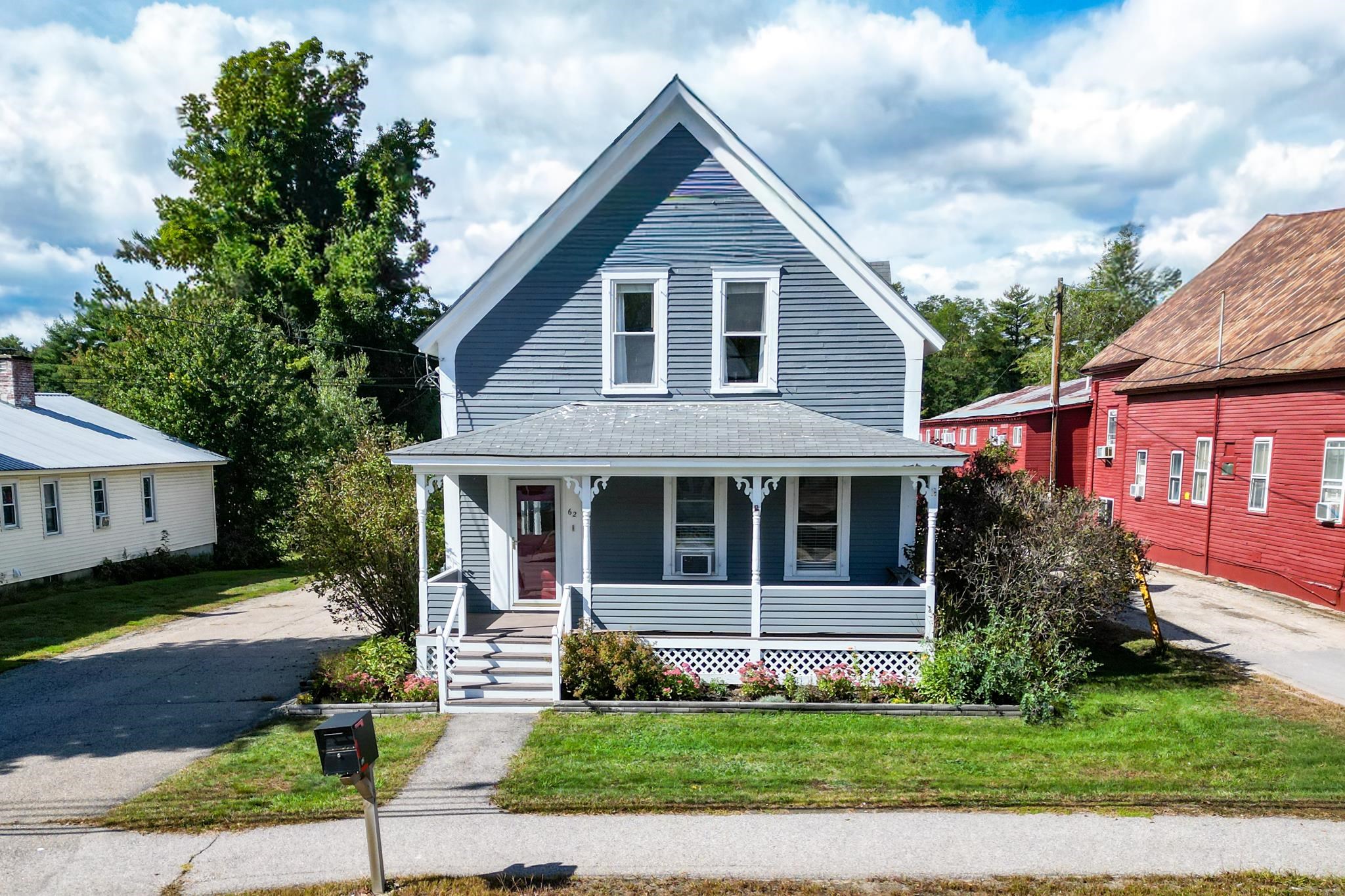 Blue-gray two-story house with a steep gabled roof, white-trimmed porch, and flower beds.