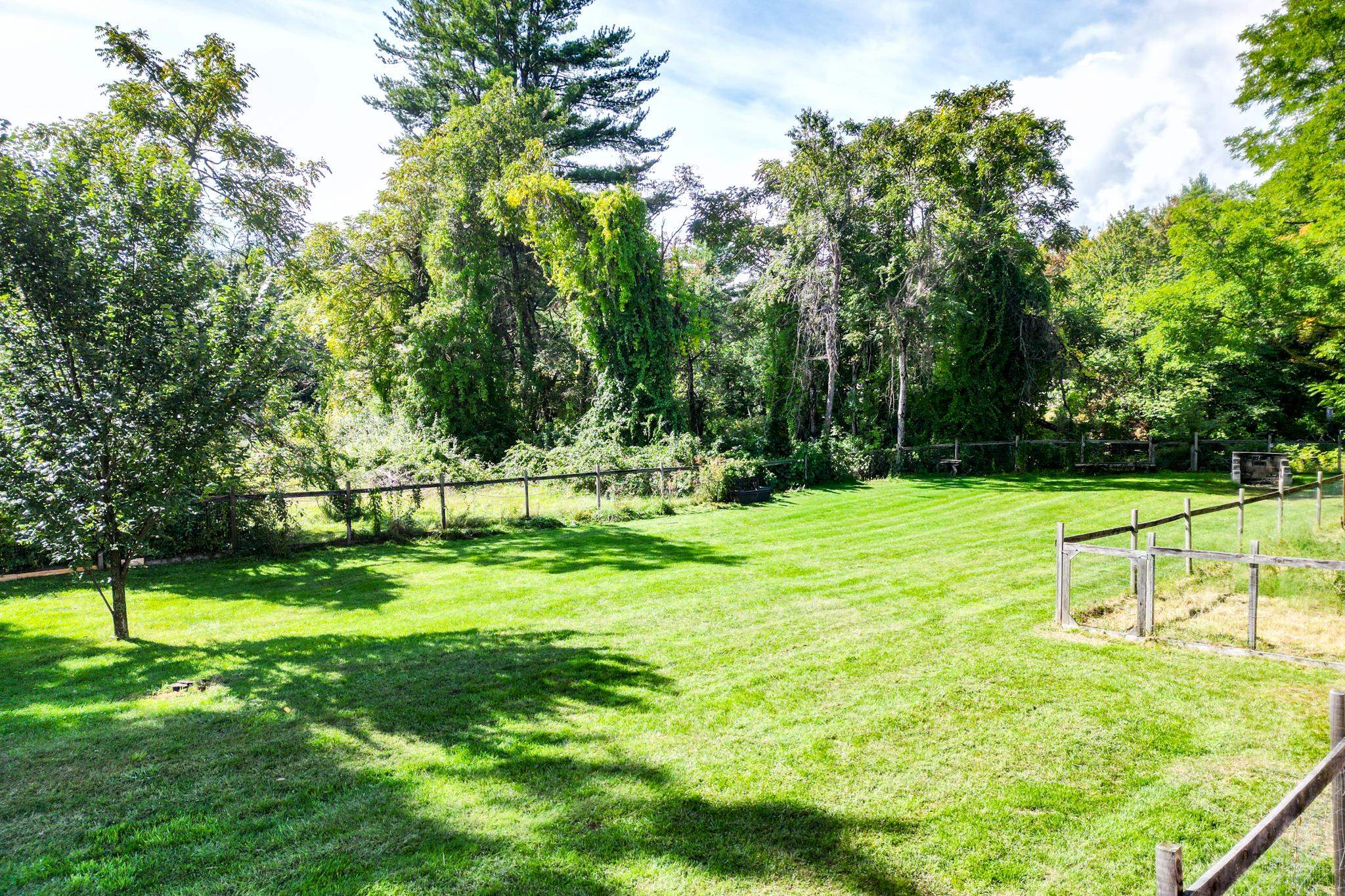 Spacious green lawn bordered by rustic fences and mature trees.