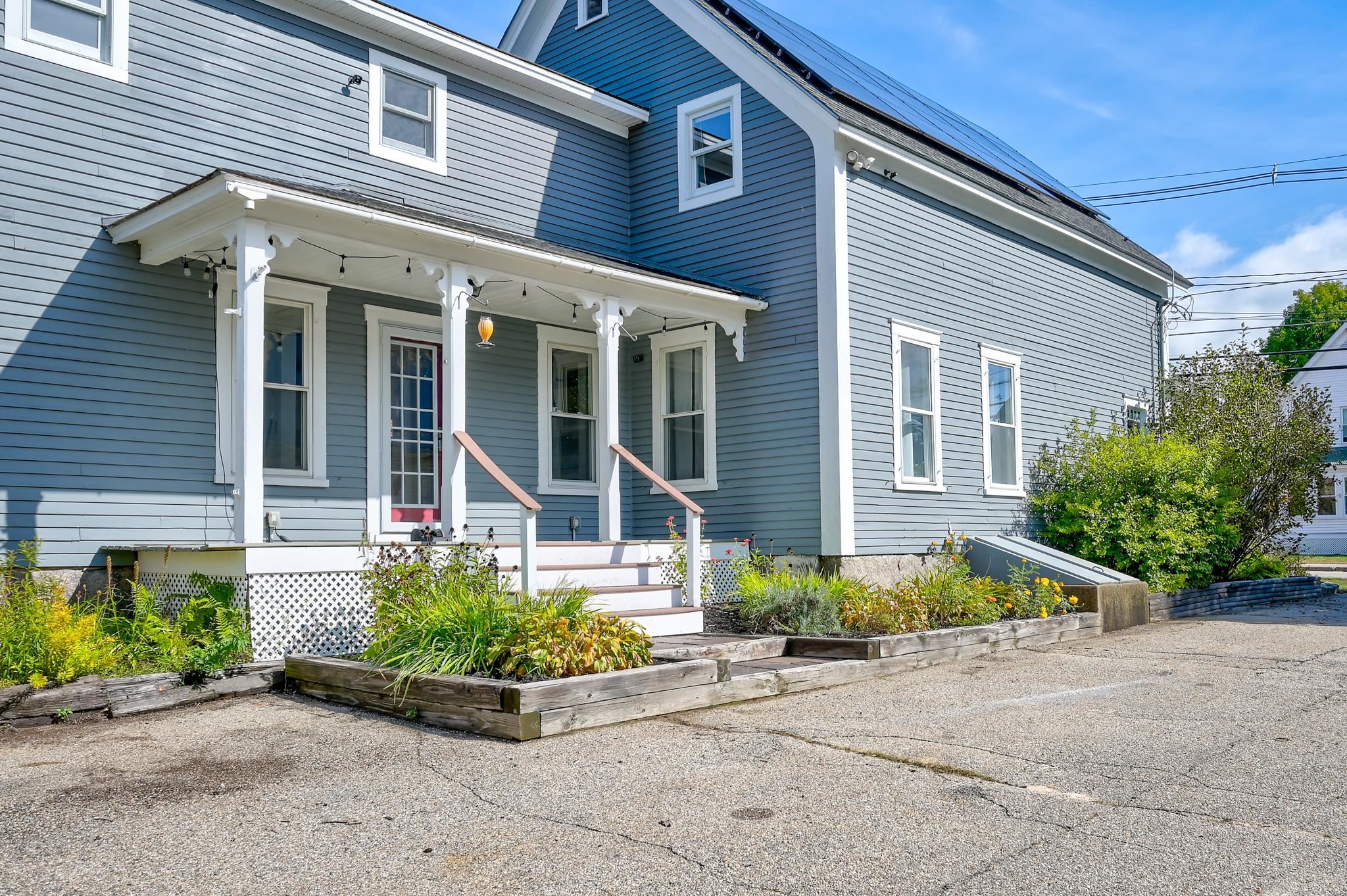 Blue-gray house with a covered porch, rooftop solar panels, and raised flower beds.