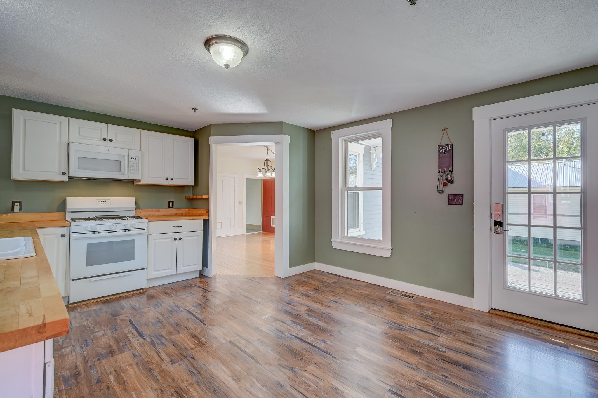 Kitchen with white cabinets, butcher-block counters, and wood-look flooring beside a glass-paneled door.