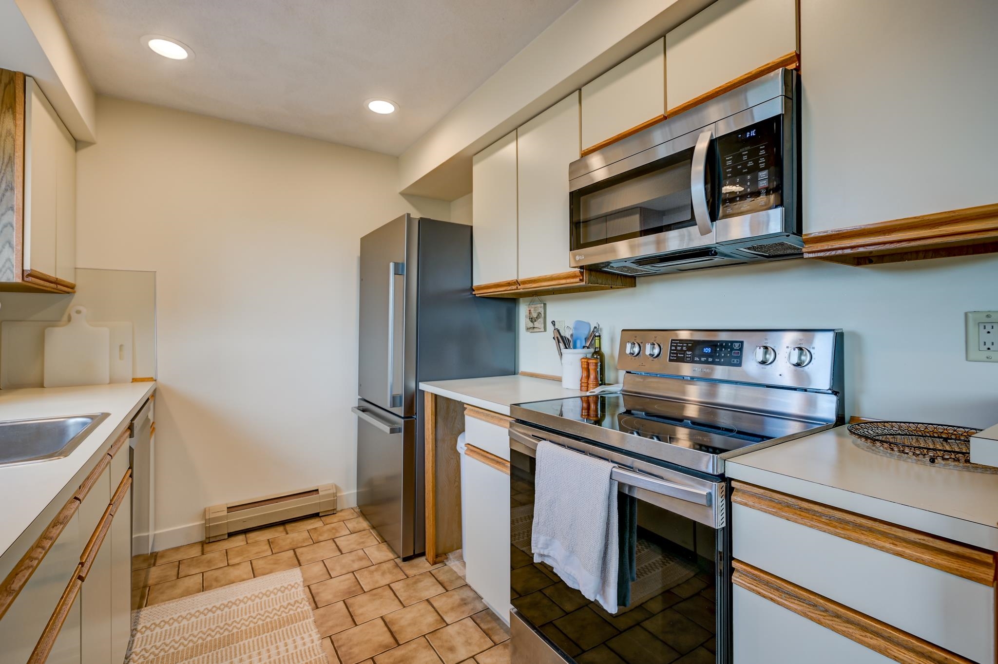 Kitchen with stainless steel appliances, white cabinets with wood trim, and tan tile flooring.