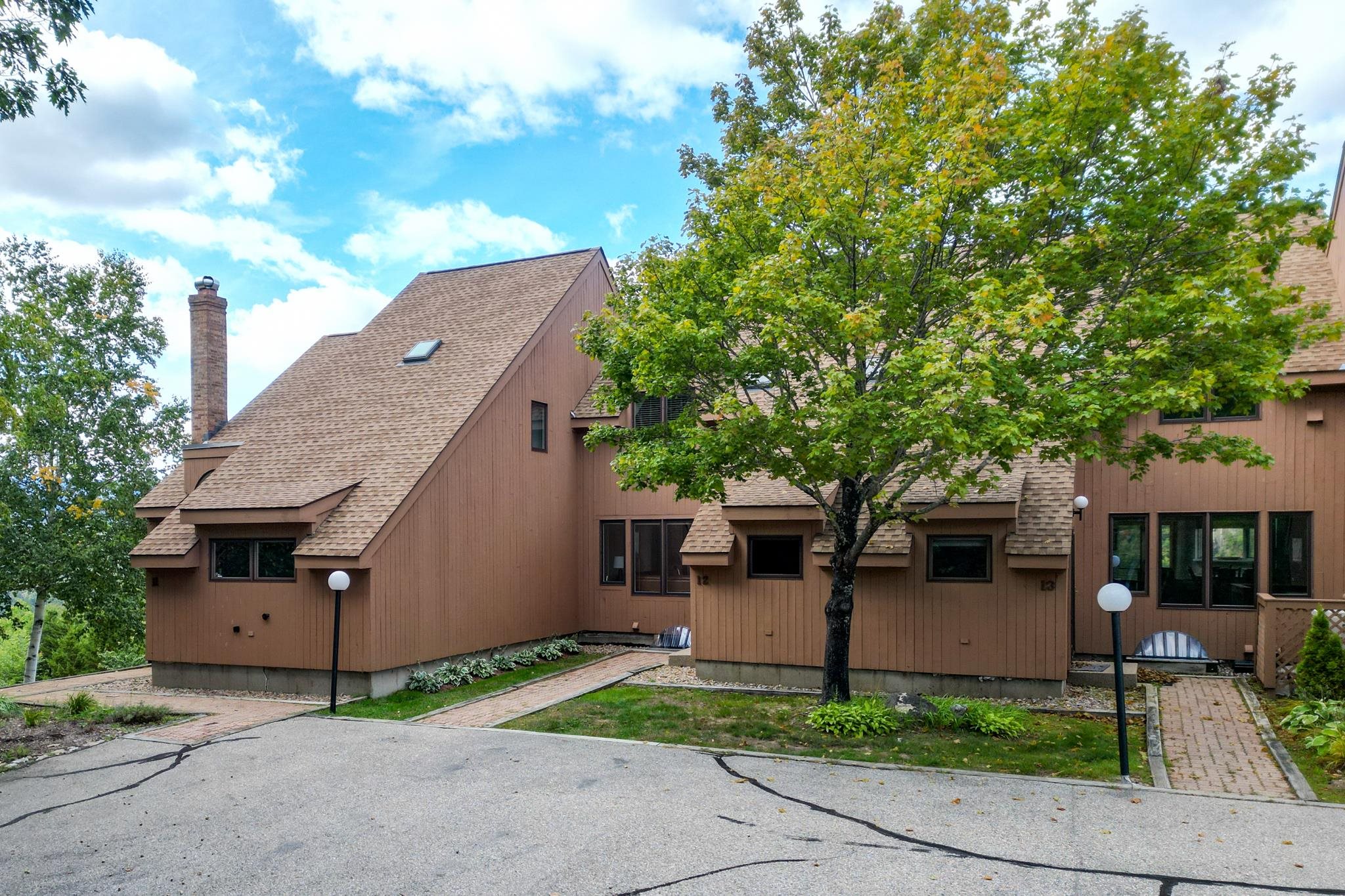 Brown-sided condominium exterior with steep roofs and a large leafy tree in front.