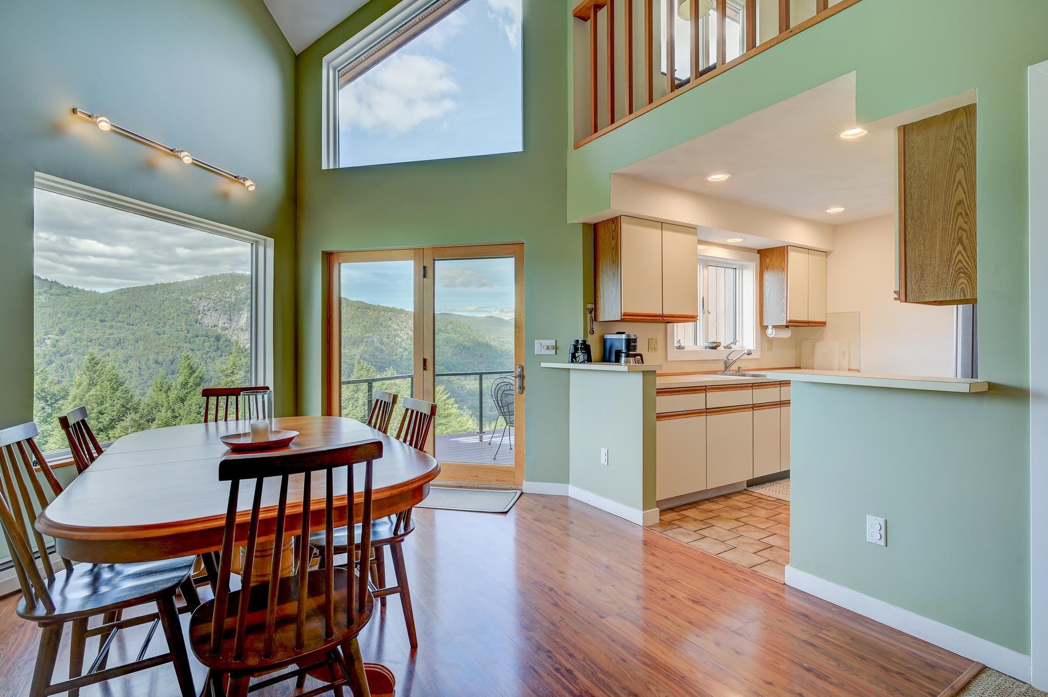 Dining area and kitchen with a high ceiling, sliding glass door, and forested mountain views.