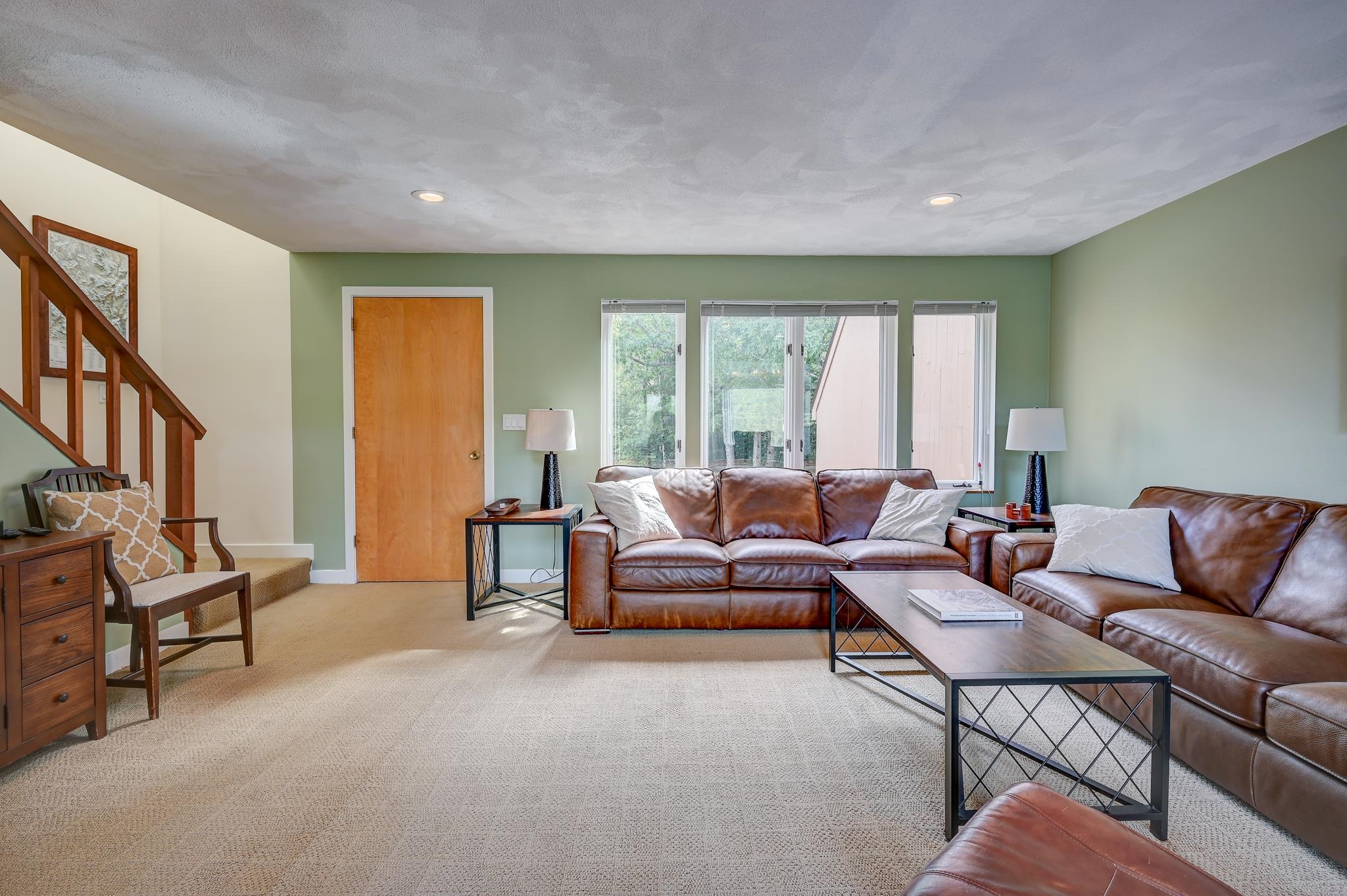 Living room with brown leather sofas, sage-green walls, and a wooden staircase.