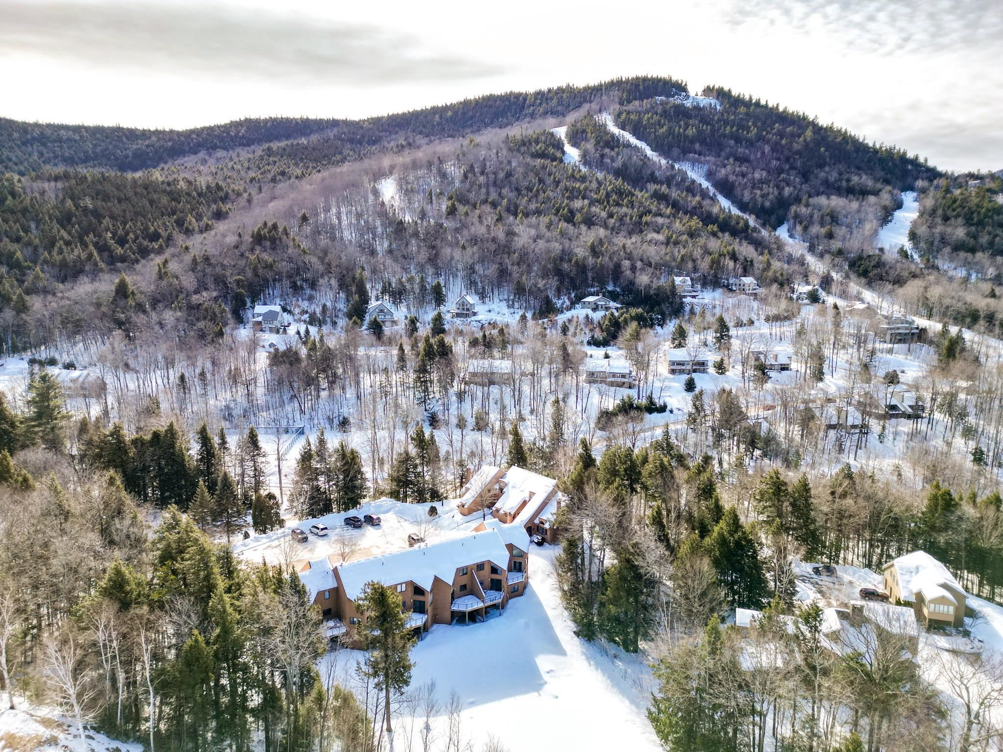 Snow-covered condominium building amid wooded hills and ski trails.