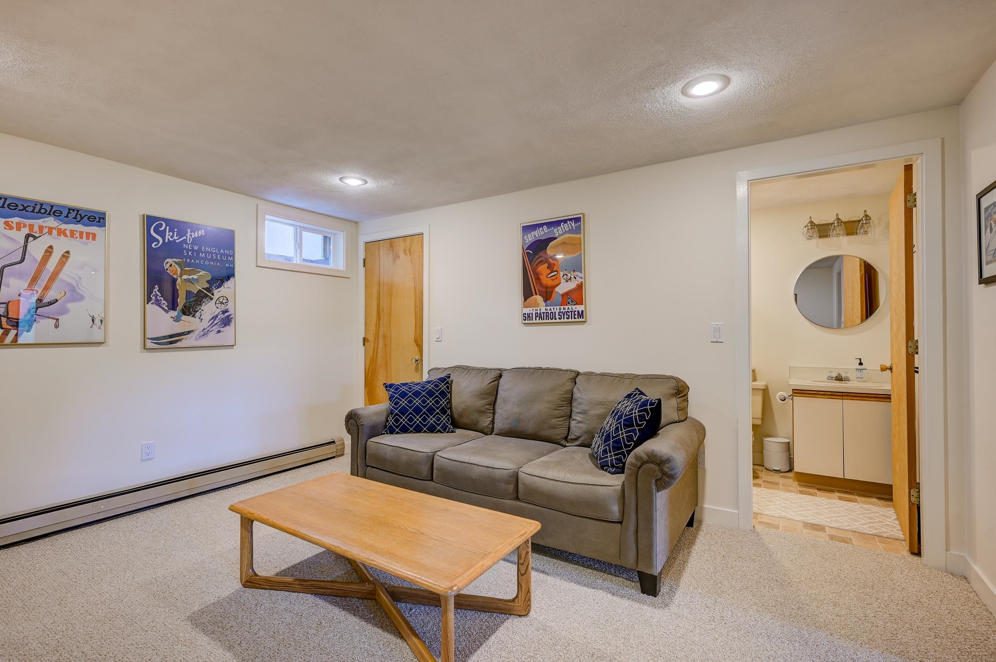 Furnished living room with a gray sofa, wooden coffee table, ski posters, and an adjoining bathroom.