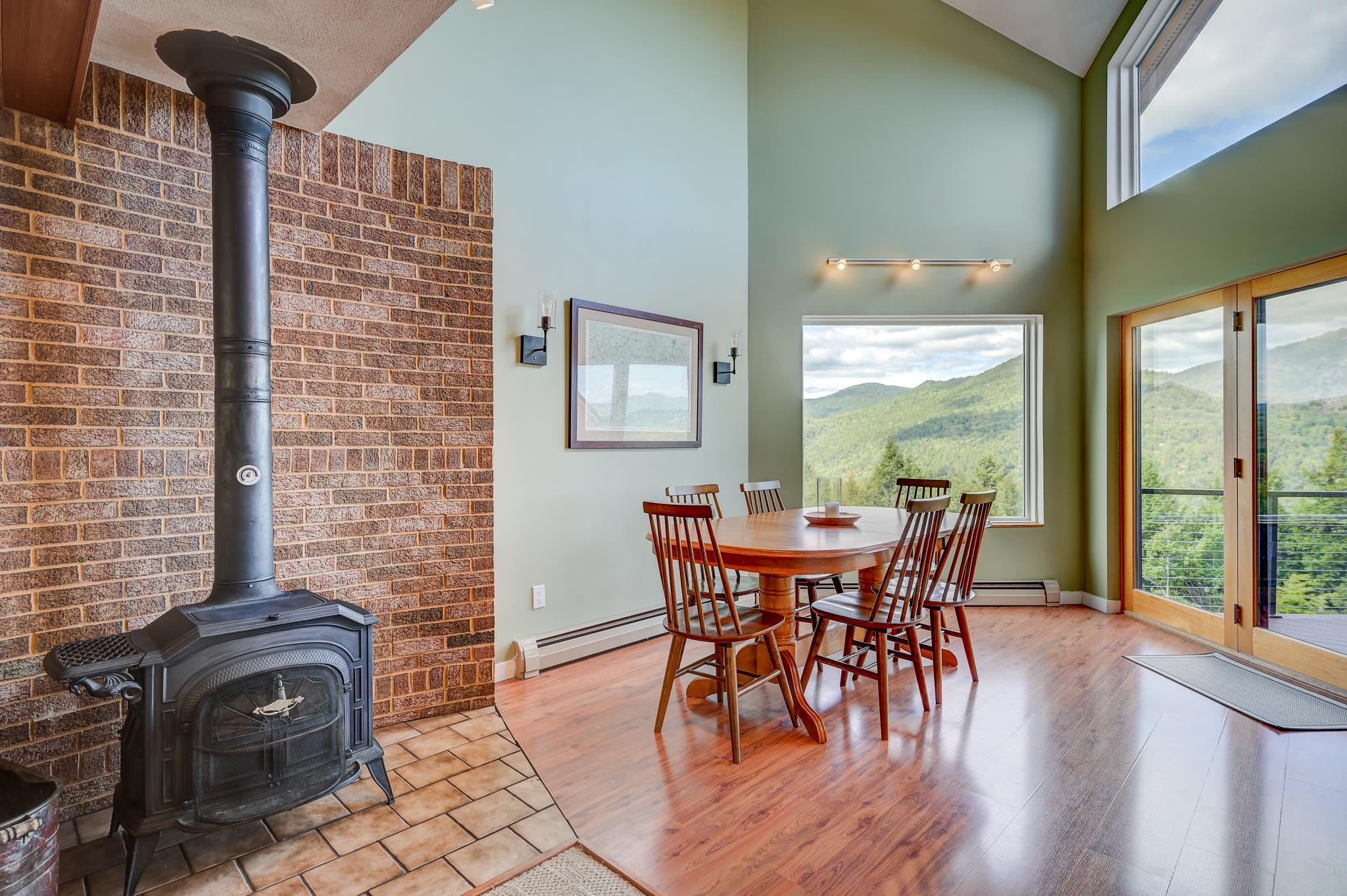 Dining area with a brick-backed wood stove, round wooden table, and mountain views.