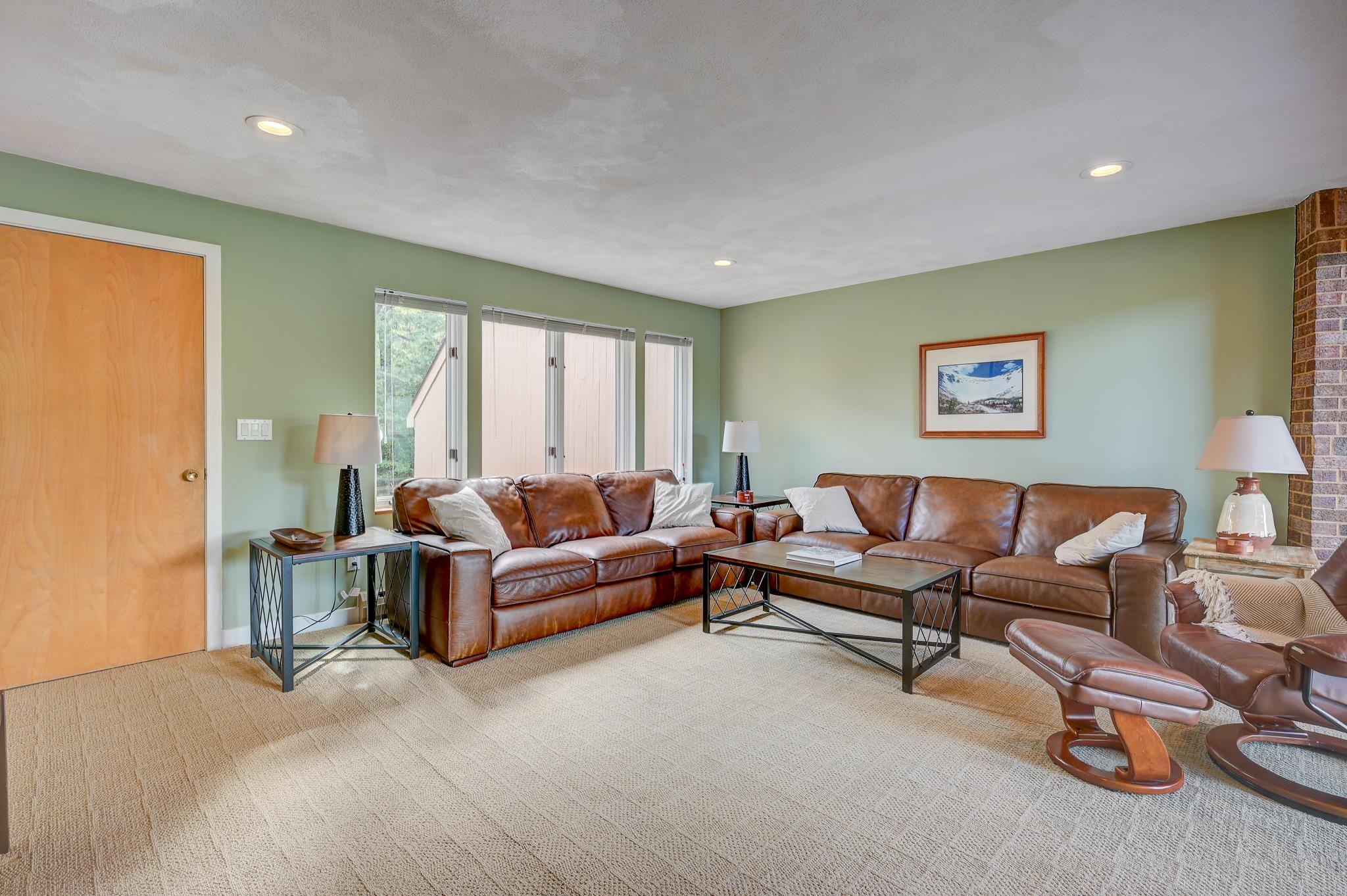 Living room with brown leather sofas, sage-green walls, and a brick fireplace.