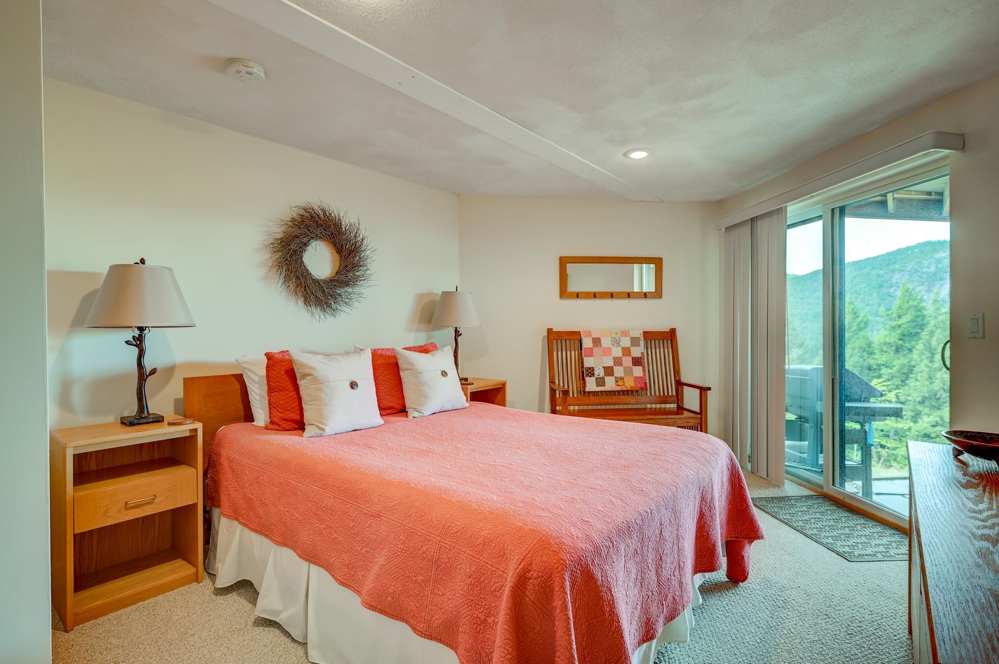 Bedroom with a coral quilt and sliding glass doors overlooking a green mountain.