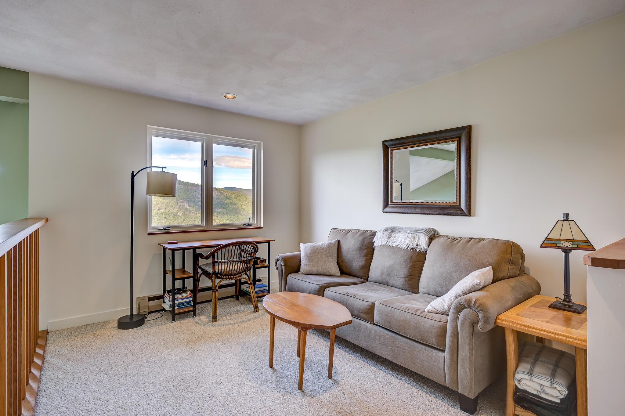 Furnished living room with gray sofa, mountain view through twin windows, and wood furniture.