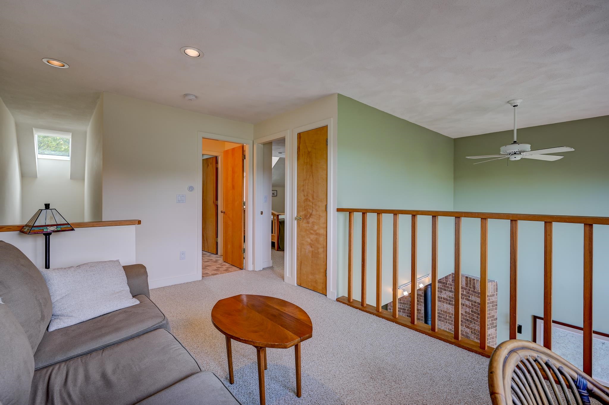 Upstairs sitting area with a gray sofa and wooden railing overlooking the lower level
