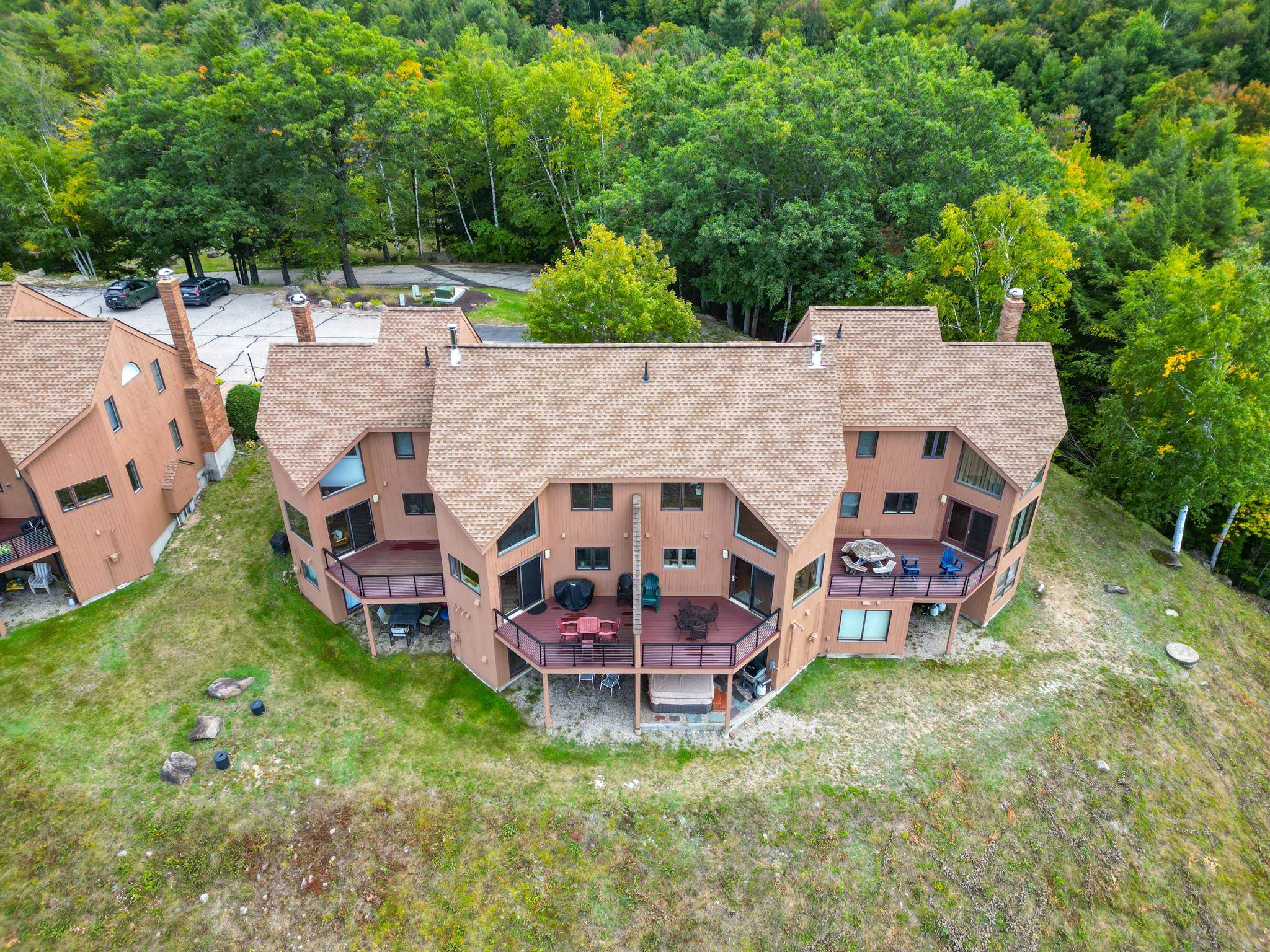 Aerial view of a brown condominium building with furnished decks beside a wooded area.