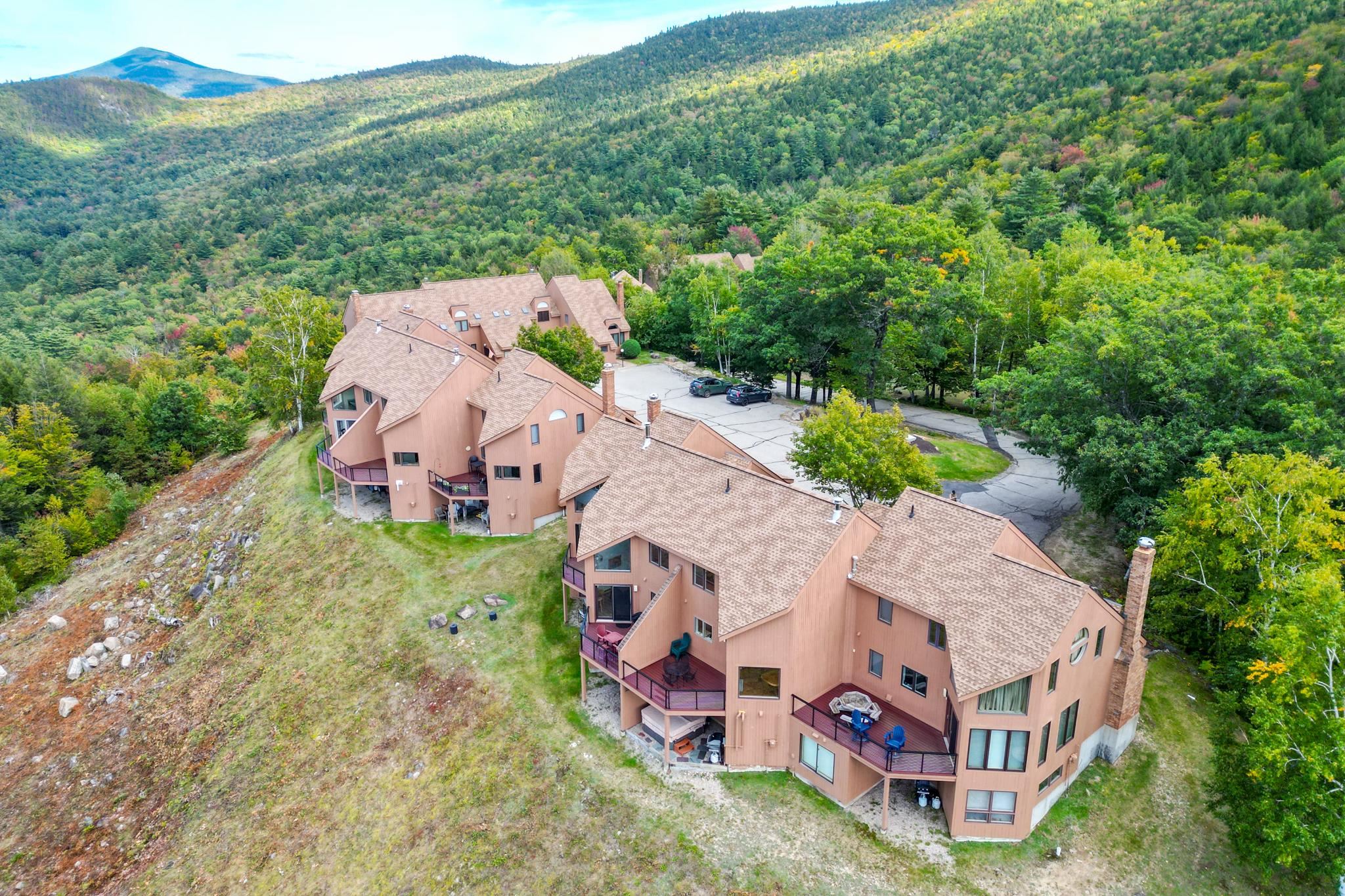 Aerial view of a condominium complex with balconies, surrounded by wooded mountain slopes.