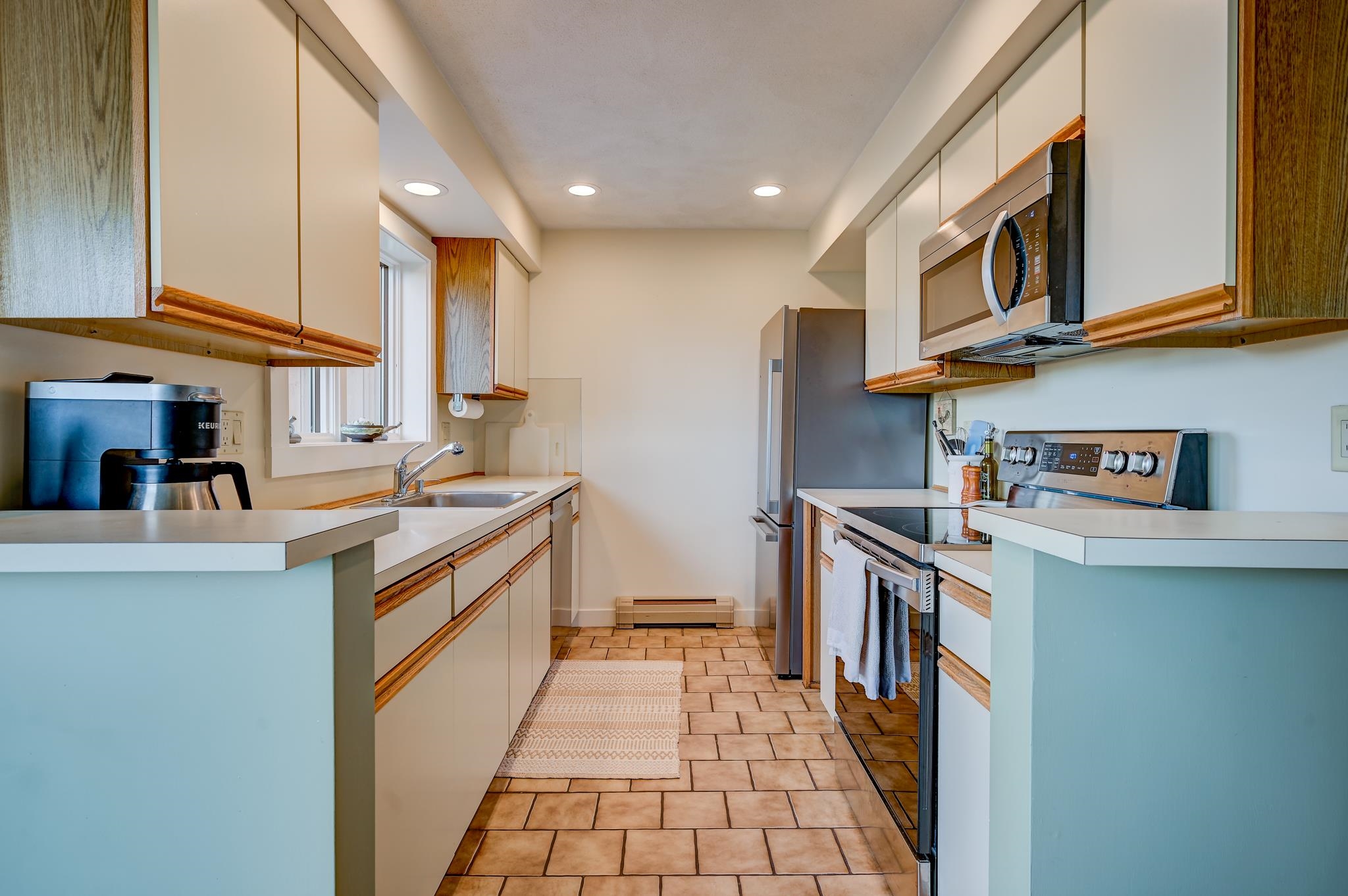 Galley kitchen with cream and wood-trimmed cabinets, tile floors, and stainless-steel appliances.
