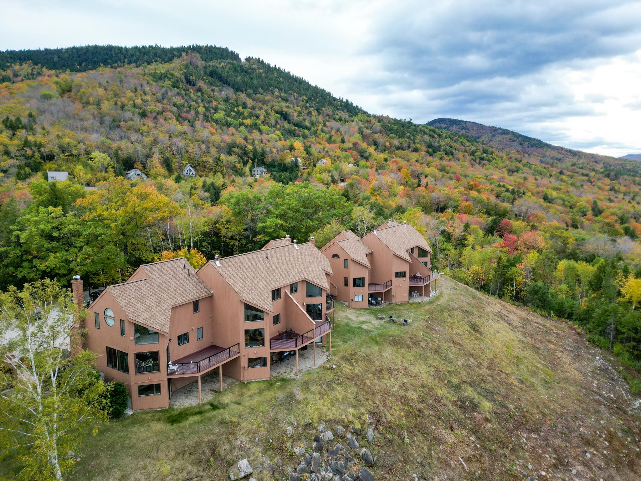 Aerial view of a brown multi-unit building with decks against an autumn mountain forest.