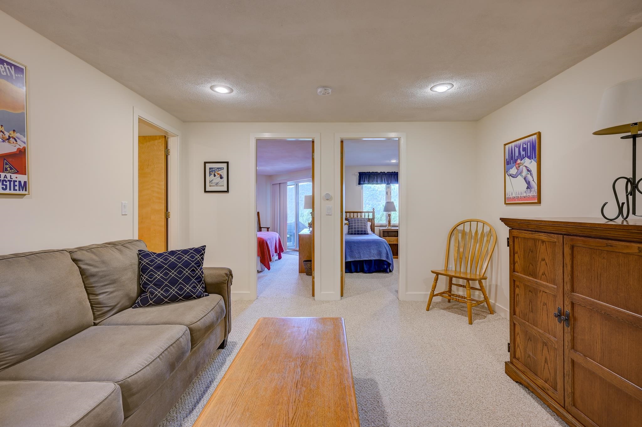 Furnished living room with a gray sofa and wooden cabinet, looking through two doorways into bedrooms.