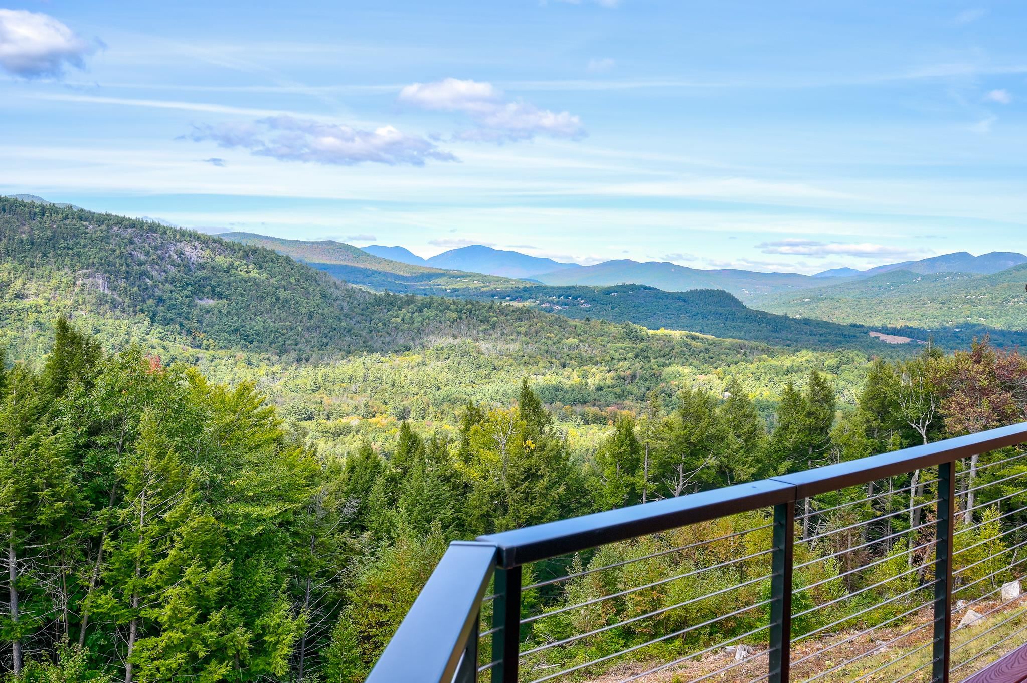 Forested mountain view from a balcony, with a dark metal railing in the foreground.