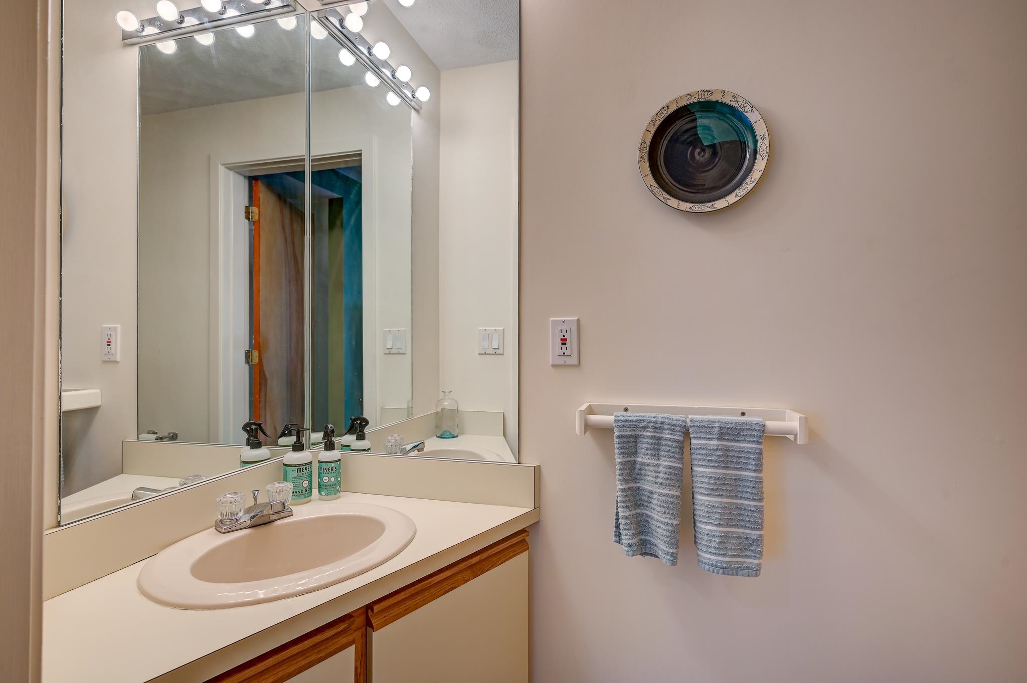 Bathroom vanity with an oval sink, large illuminated mirror, and two blue-gray towels.