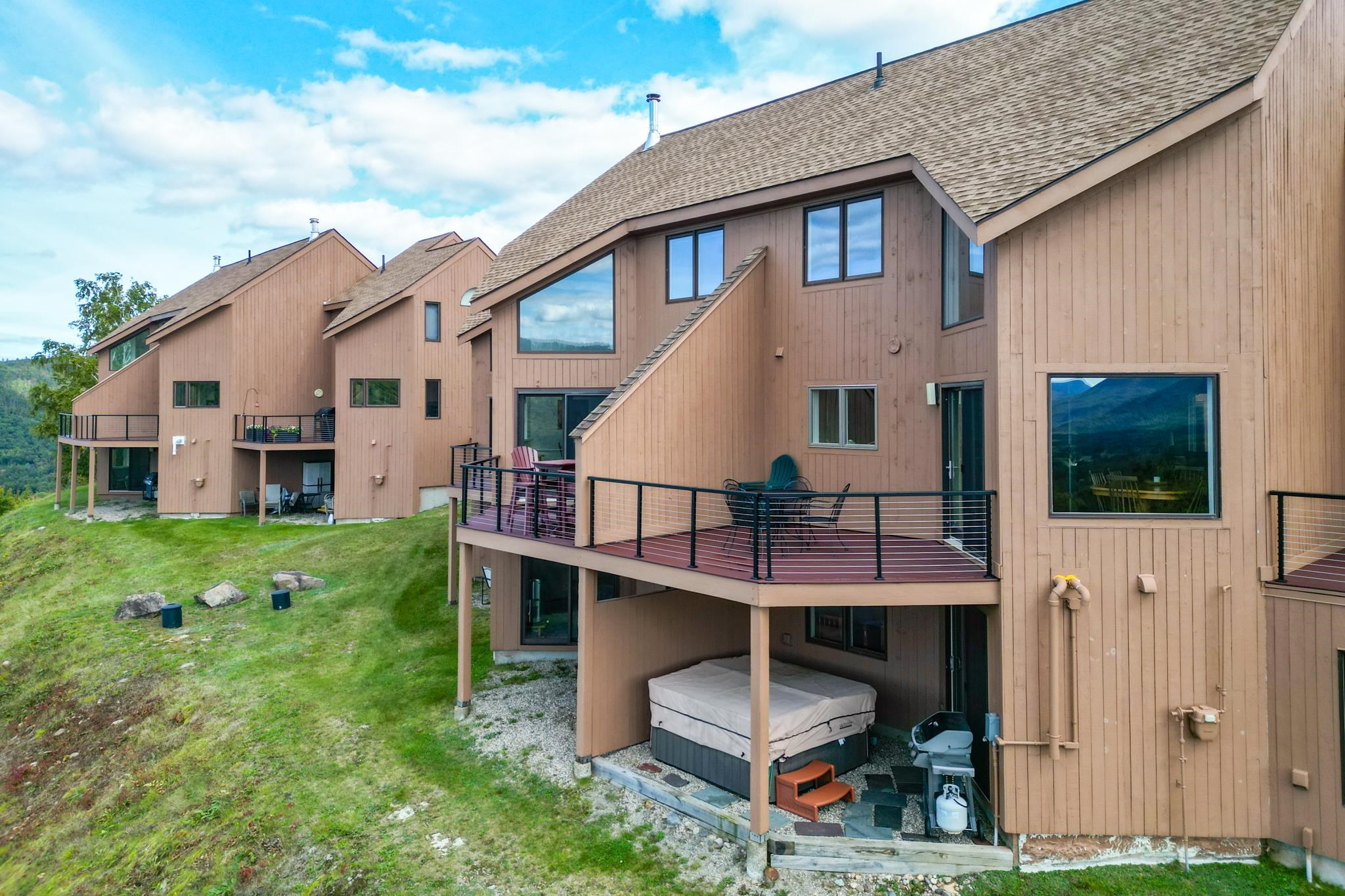 Brown hillside condominiums with raised decks and a covered hot tub beneath the nearest deck.