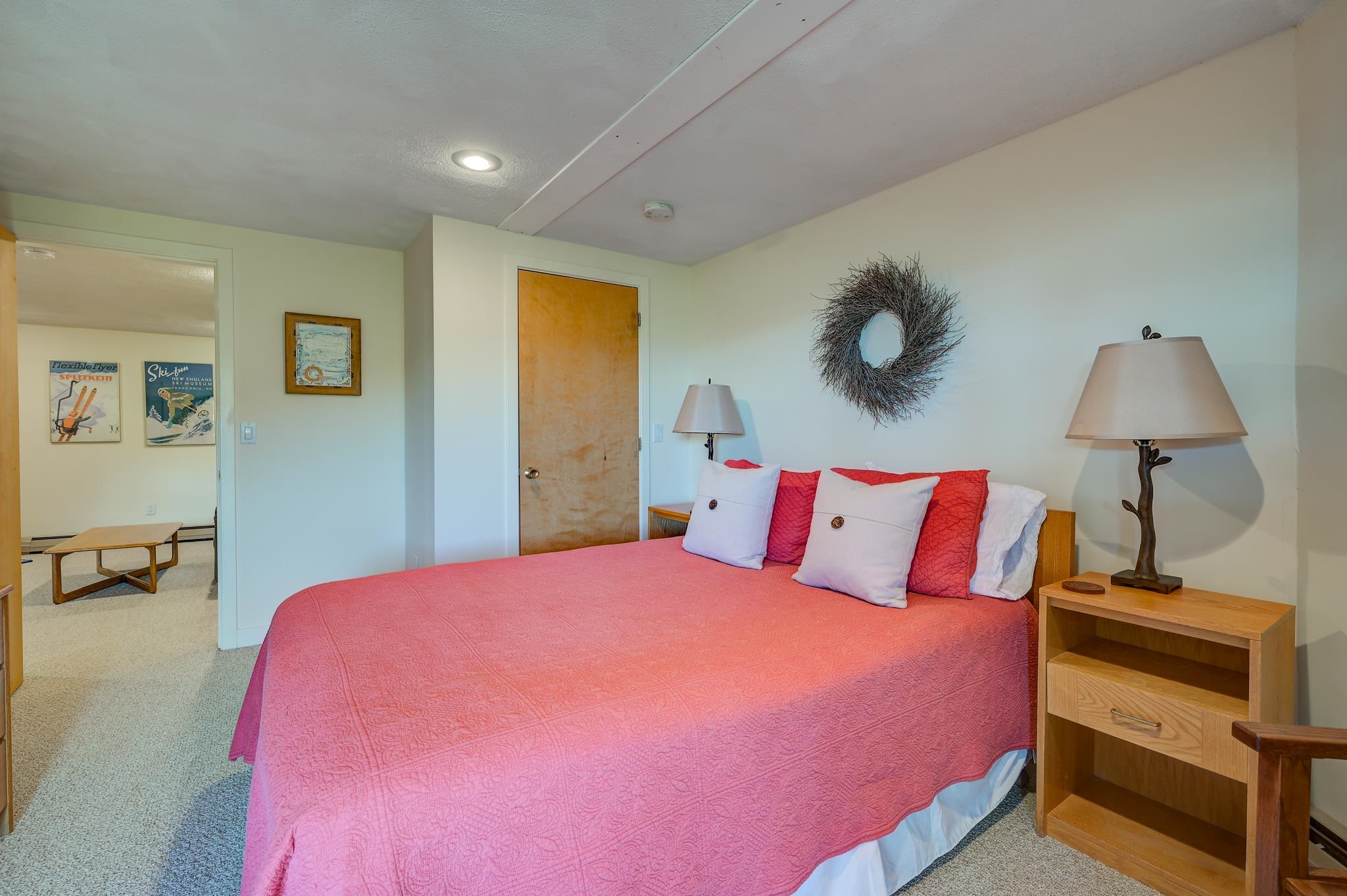 Bedroom with a pink quilted bed, twig wreath, and open doorway to a sitting area.