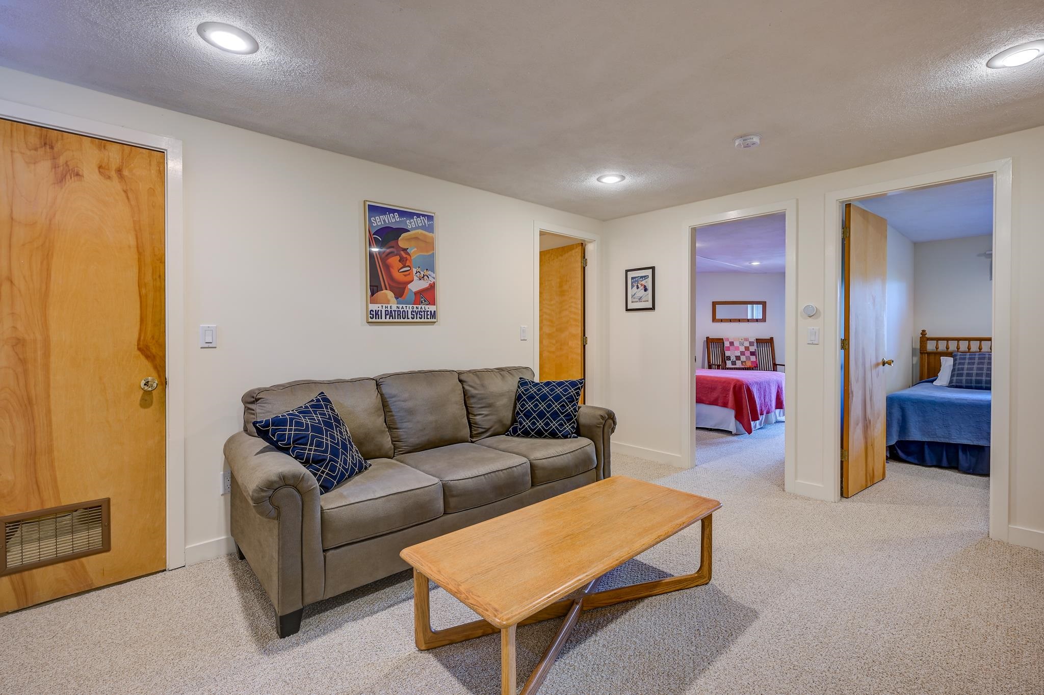 Furnished living room with a gray sofa and wooden coffee table; two bedrooms are visible through open doorways.
