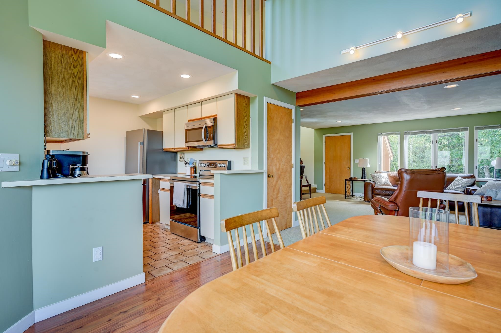 Open-plan kitchen and living room with a wooden dining table, leather seating, and loft railing.