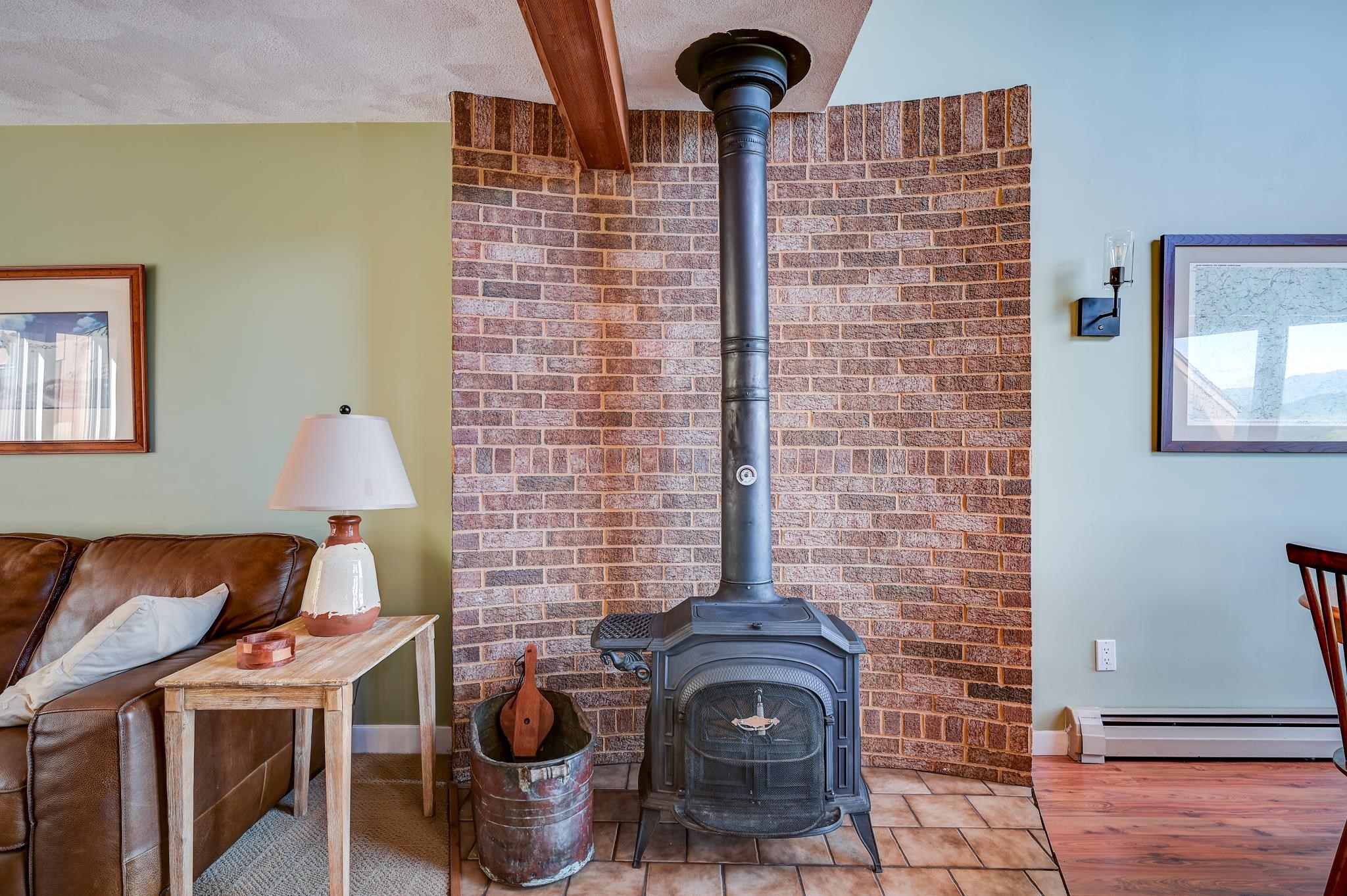Living room wood stove set against a brick wall, beside a leather sofa and tiled hearth.