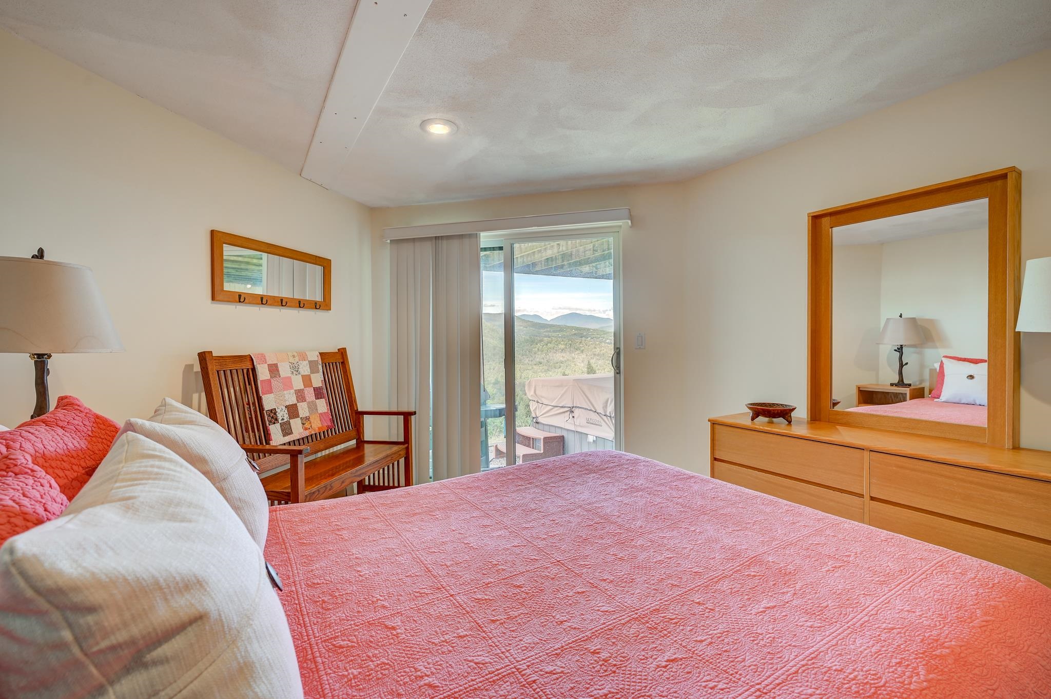 Bedroom with a coral quilt, wooden furnishings, and mountain views through the sliding glass door.