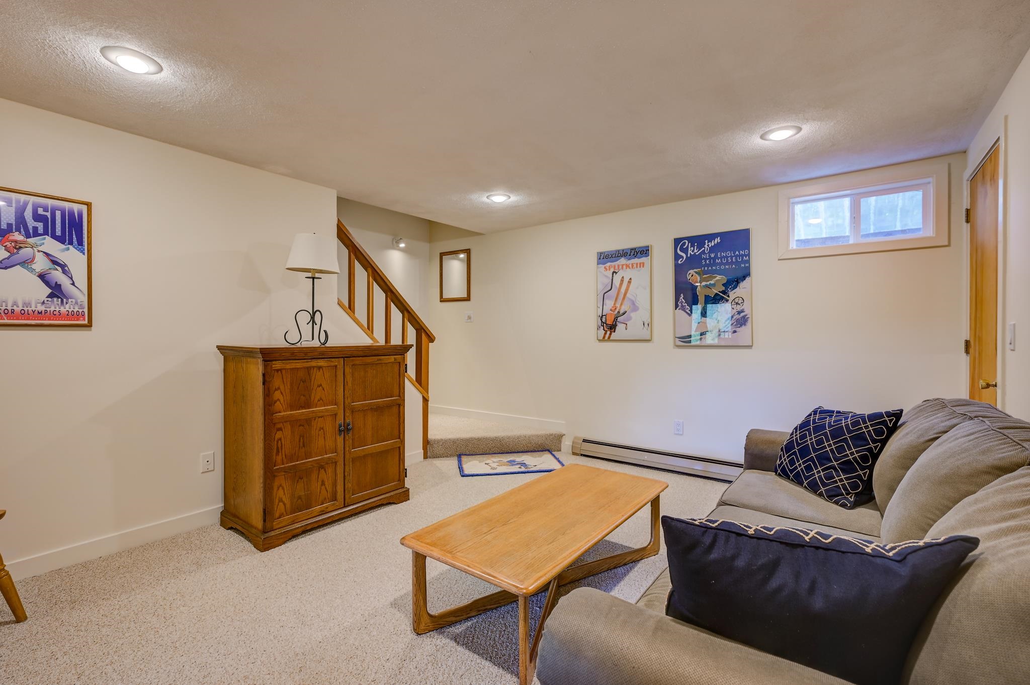 Living room with gray sectional, wooden coffee table, carpeted stairs, and vintage ski posters.