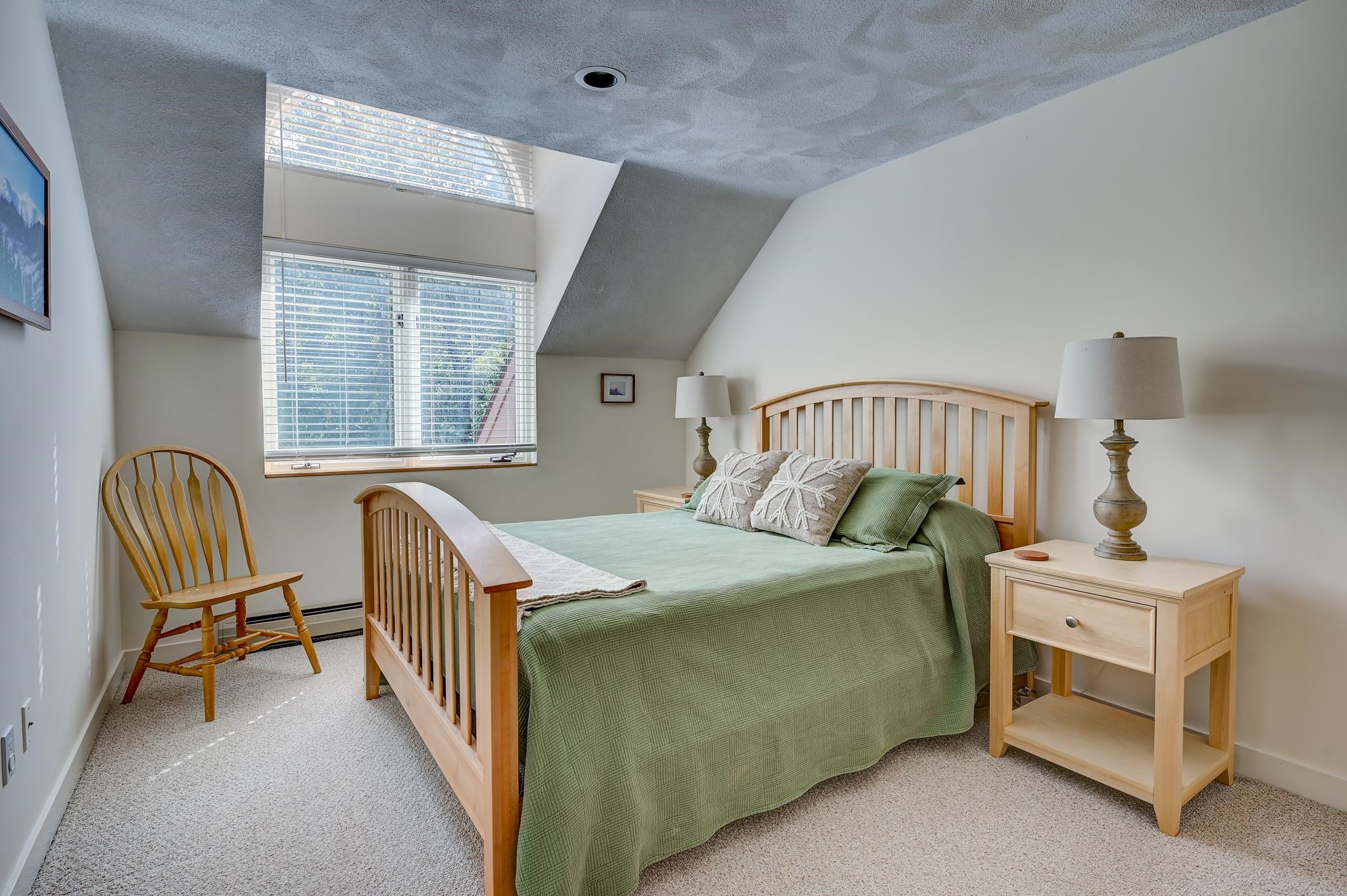 Bedroom with green bedding, a light wood bed, and a large window beneath a sloped ceiling.