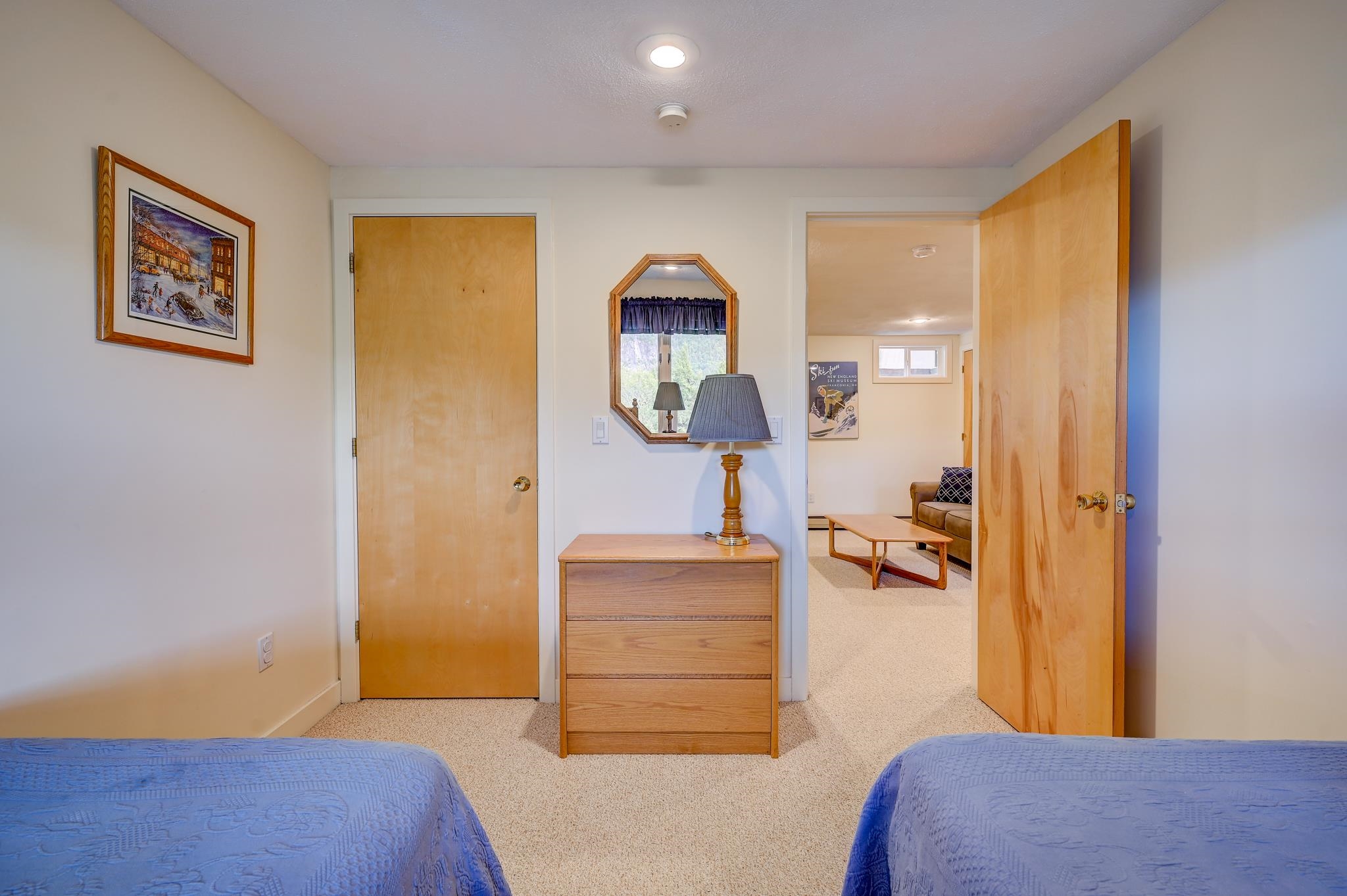 Bedroom with two blue-quilted twin beds, a wooden dresser, and an open doorway to a sitting area.