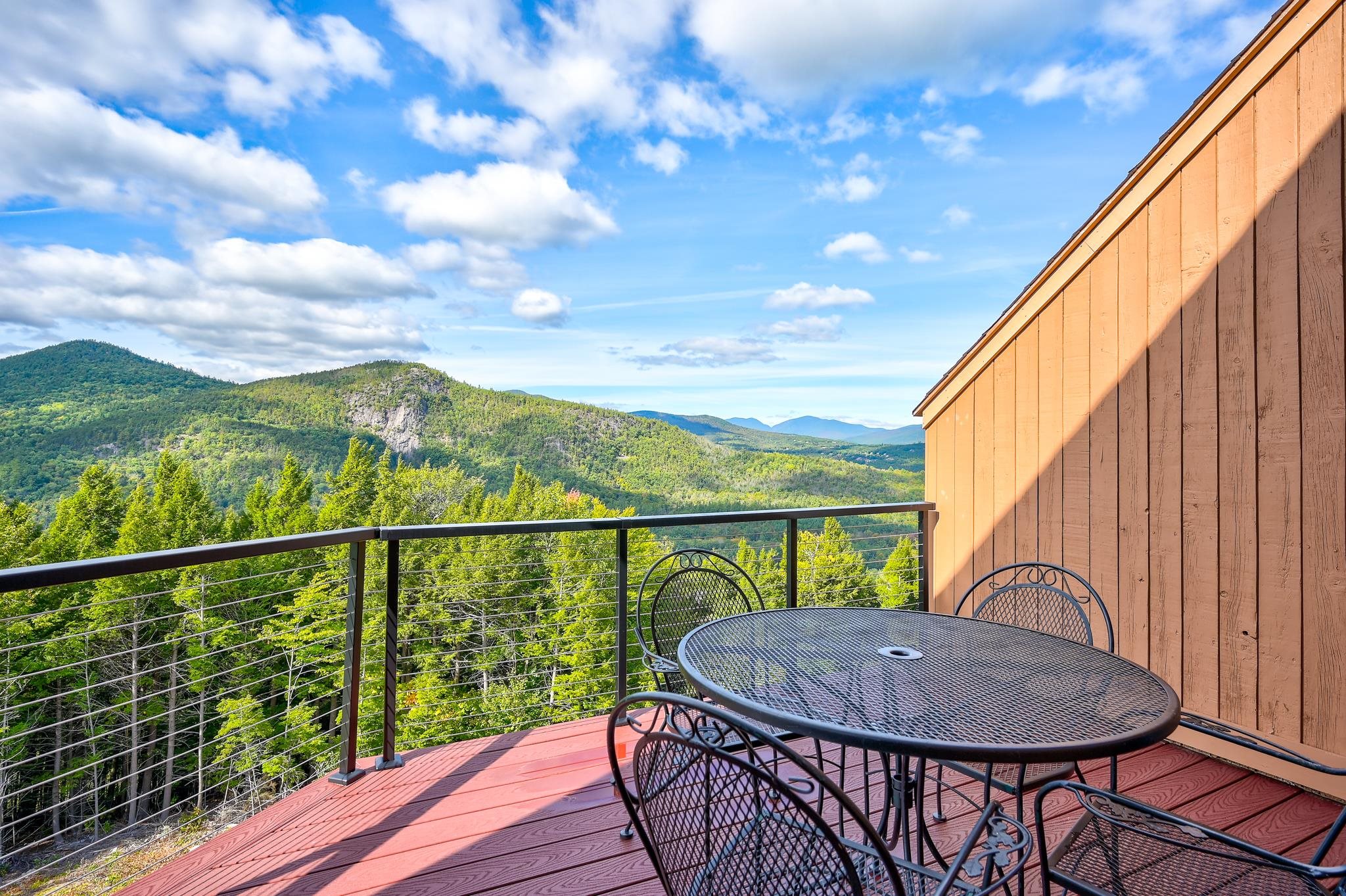Outdoor deck with metal dining set and cable railing overlooking forested mountains.