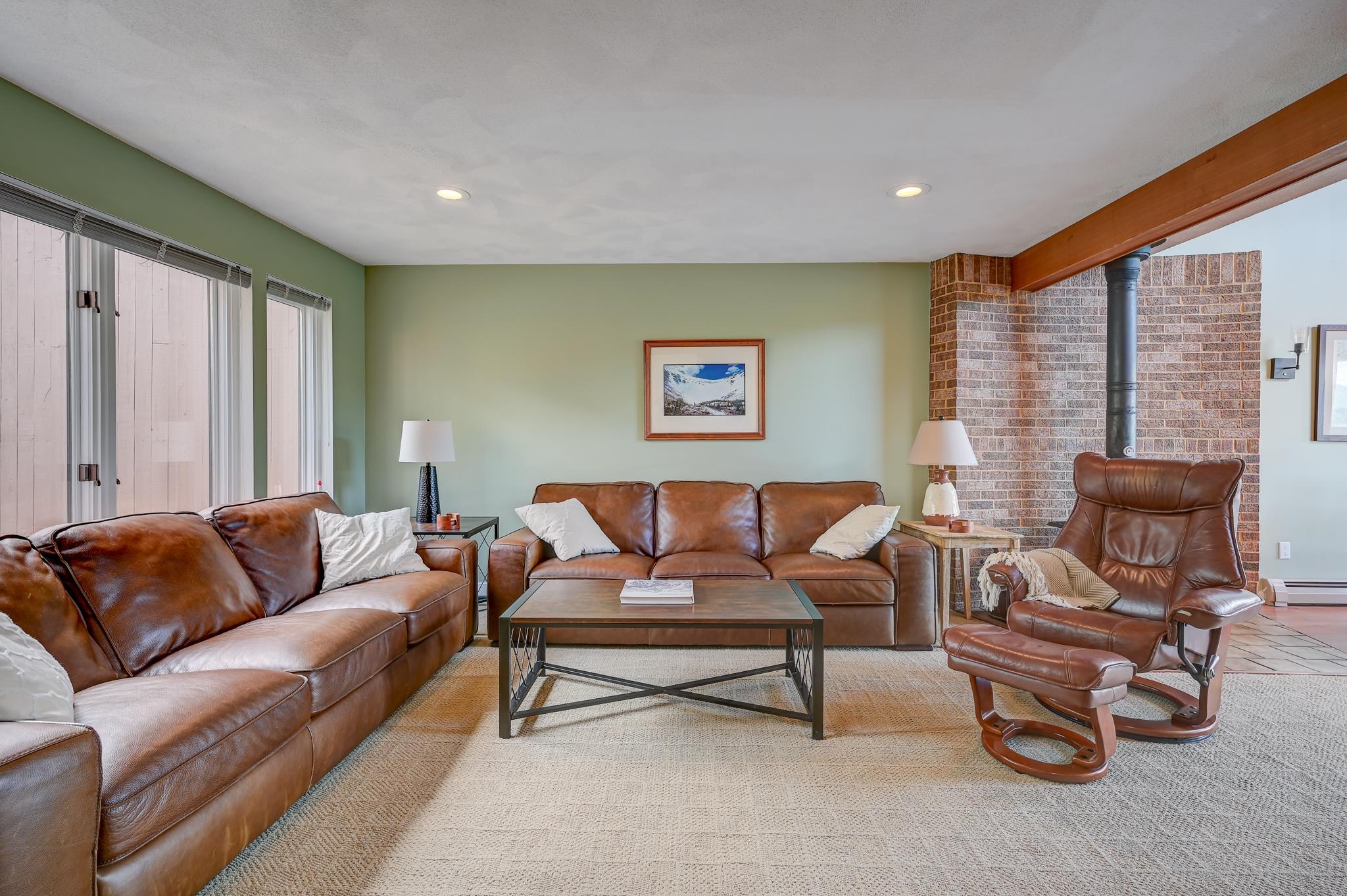 Furnished living room with brown leather seating, a brick fireplace wall, and large windows.