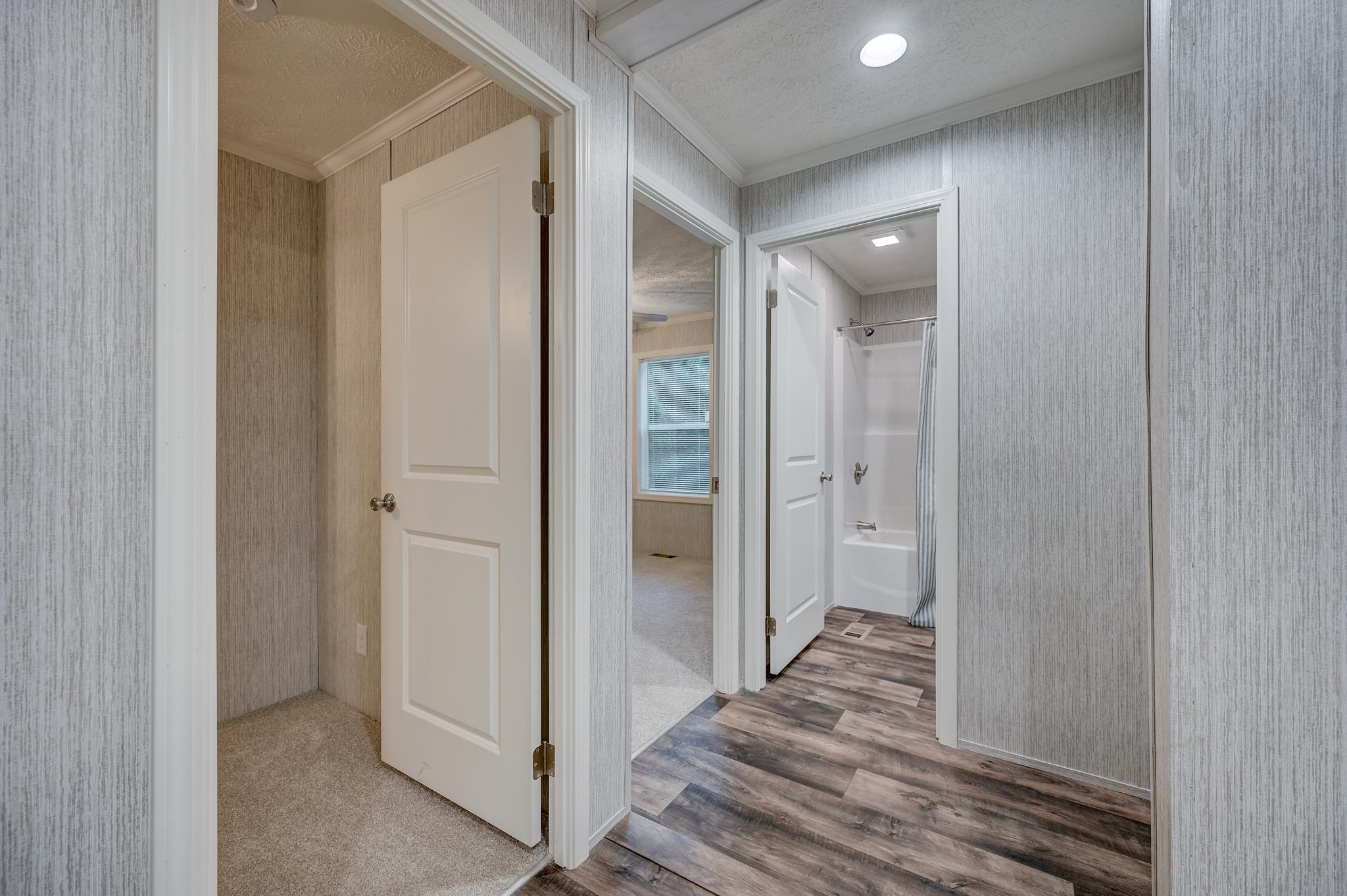 Hallway with gray plank flooring, open doorways to an empty room and a bathroom with a tub.