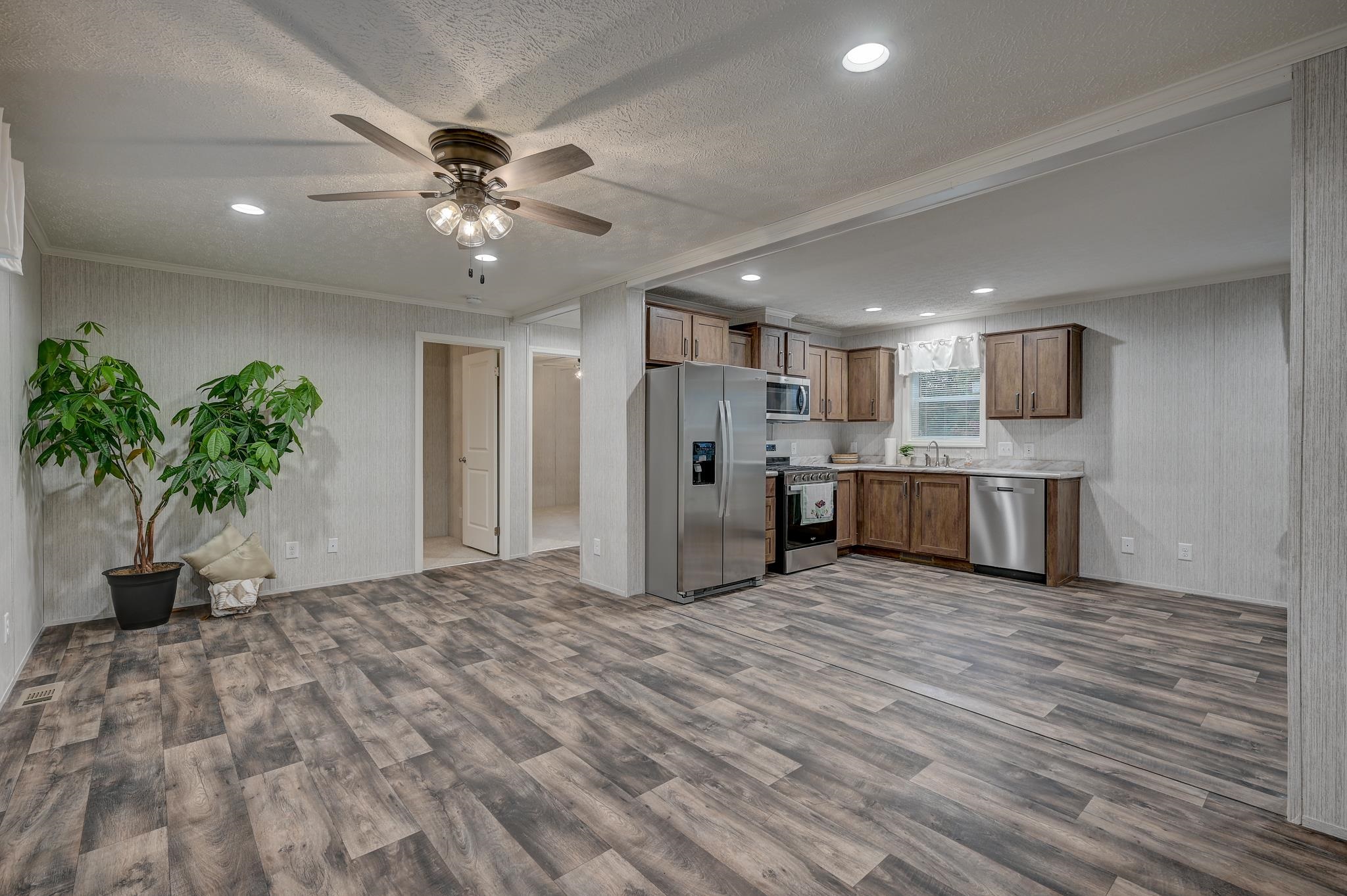 Open kitchen with wood cabinets and stainless steel appliances beside a spacious room with gray wood-look flooring.