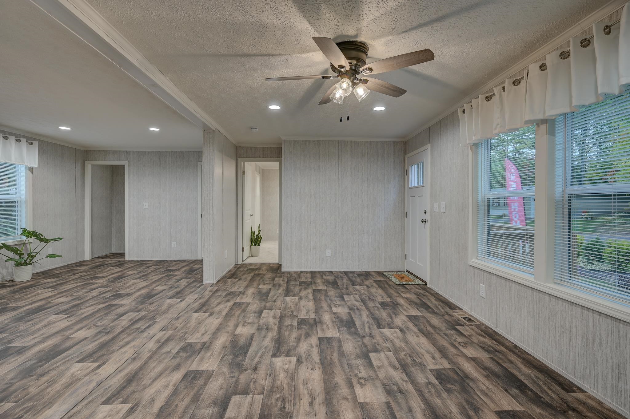 Empty living room with wood-look flooring, a ceiling fan, and large windows.