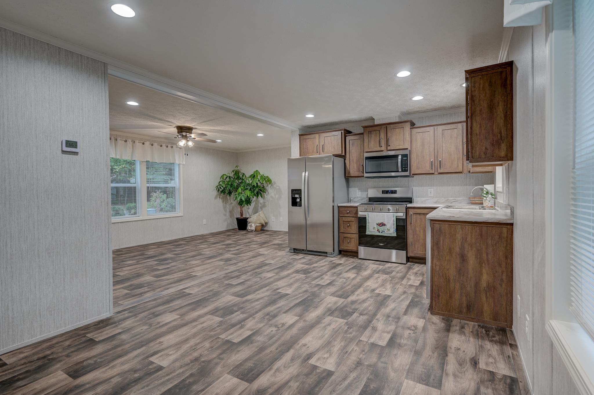 Open kitchen with wood cabinets, stainless steel appliances, and gray wood-look flooring.