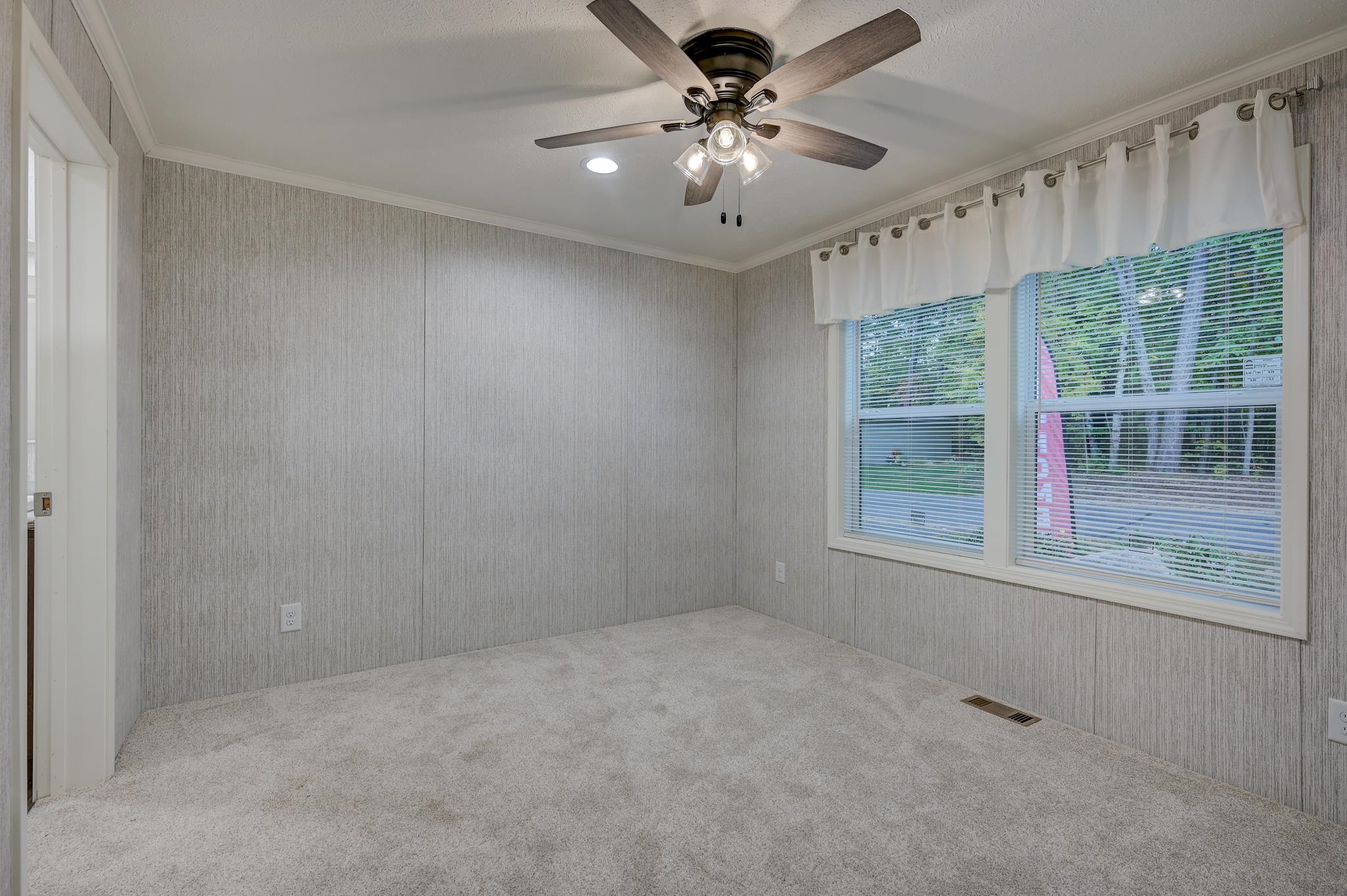 Empty carpeted room with gray walls, curtained windows, and a ceiling fan.