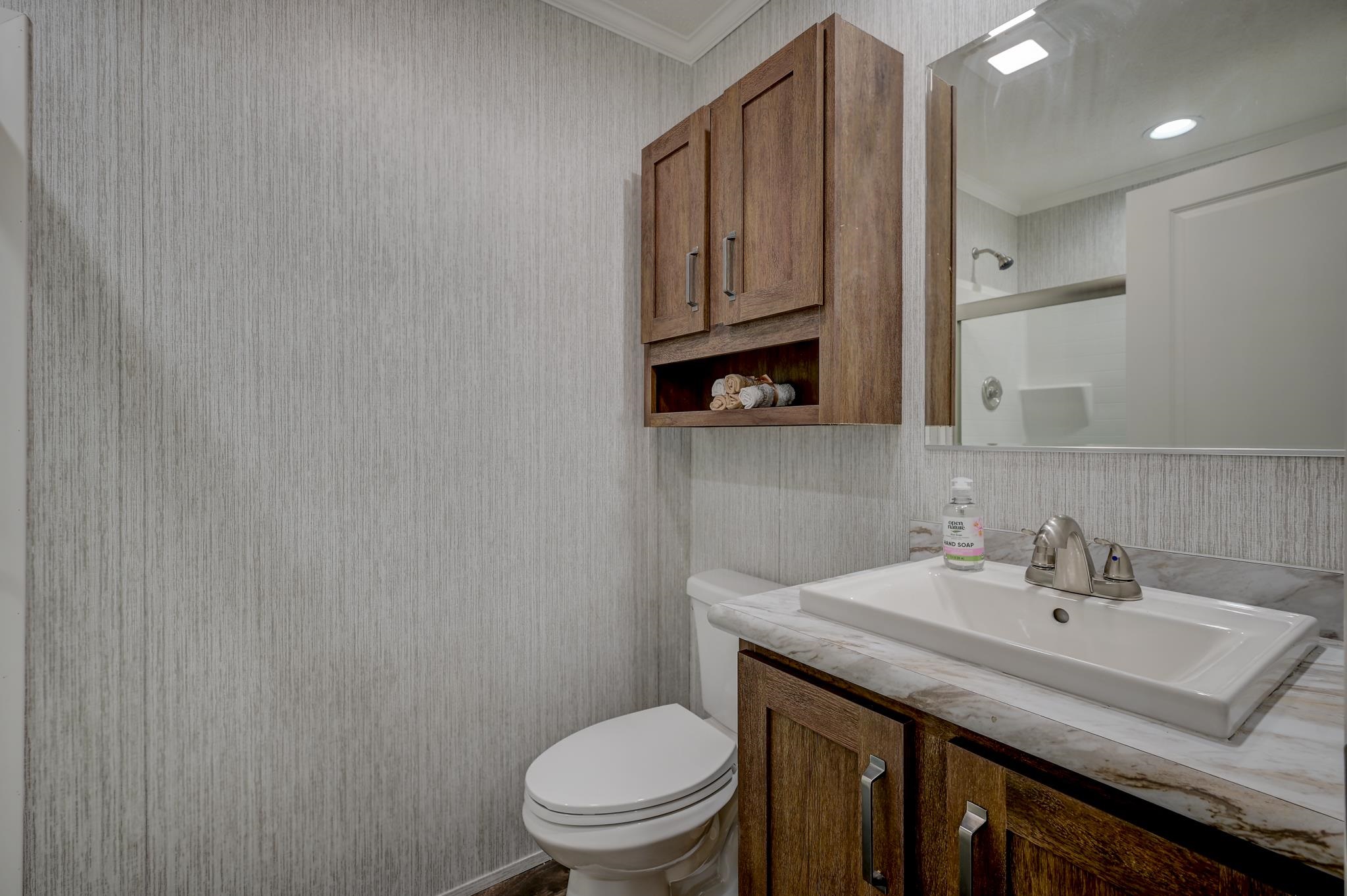 Bathroom with a dark wood vanity, marble-look counter, white sink, and wall cabinet stocked with rolled towels.