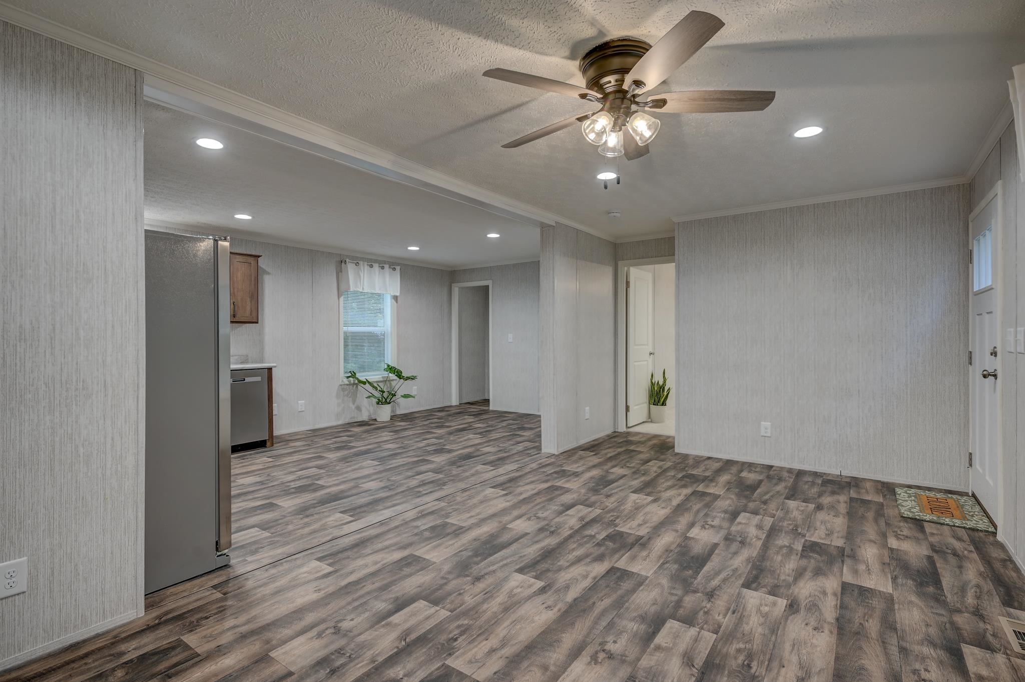 Unfurnished living room with gray wood-look floors, a ceiling fan, and a partial kitchen view.