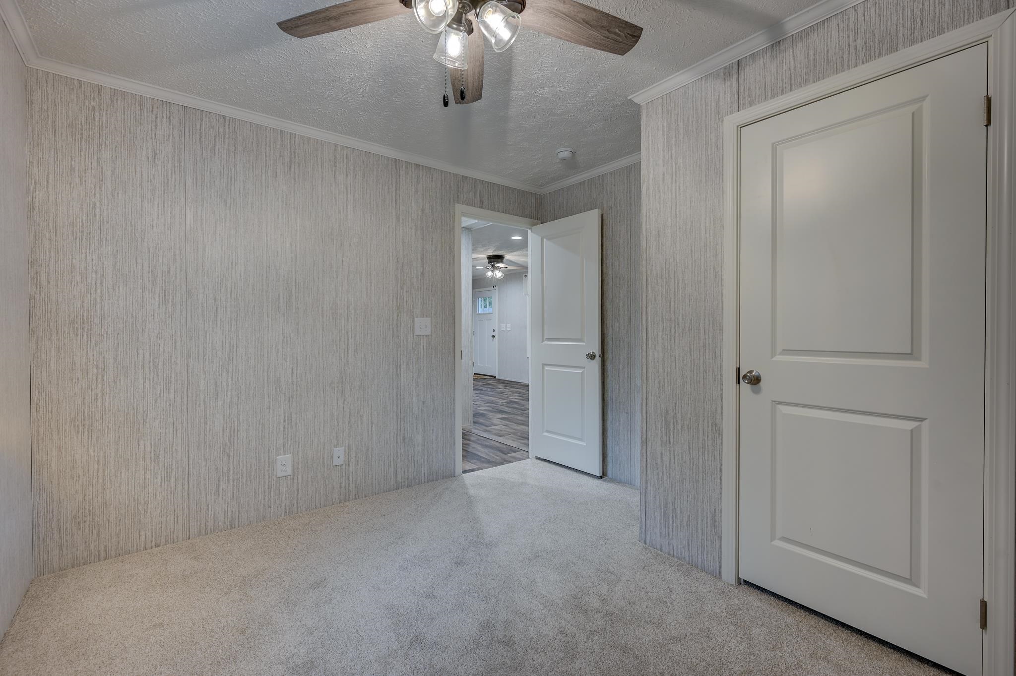 Empty carpeted room with gray wallpaper, a ceiling fan, and an open door to the hallway.