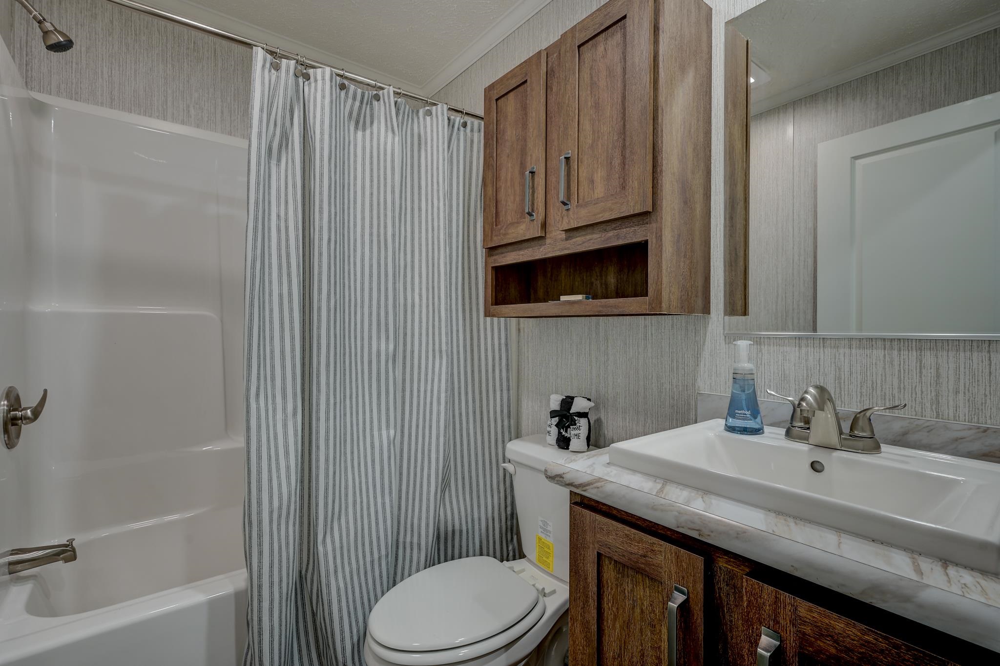 Bathroom with a striped shower curtain, white tub, toilet, and wood vanity with a wide sink.