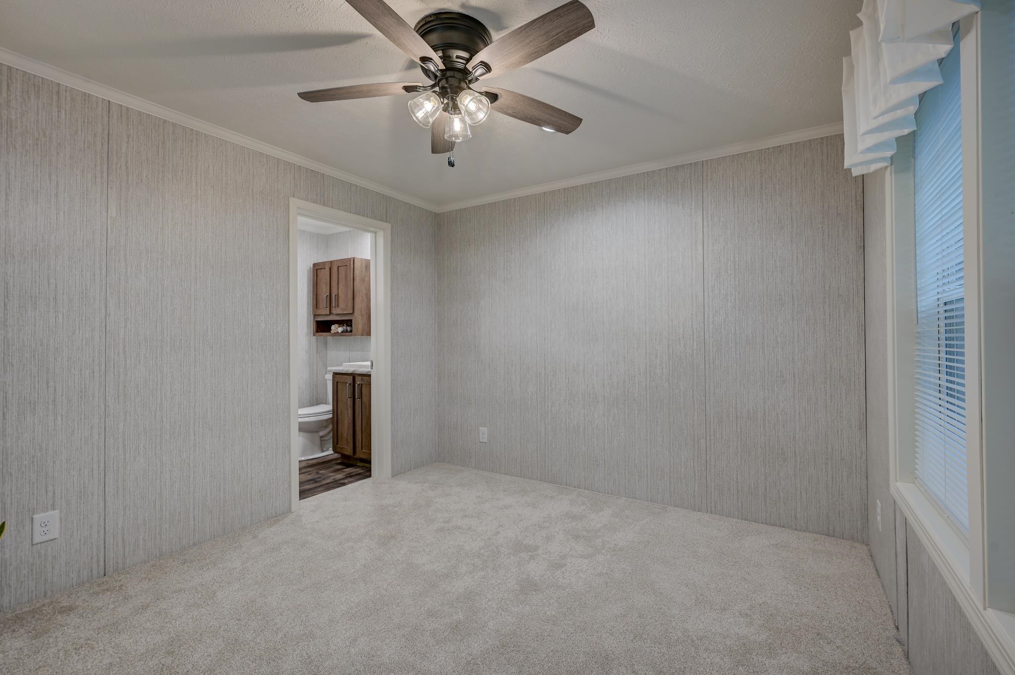 Empty bedroom with gray walls, carpet, ceiling fan, and an adjoining bathroom.