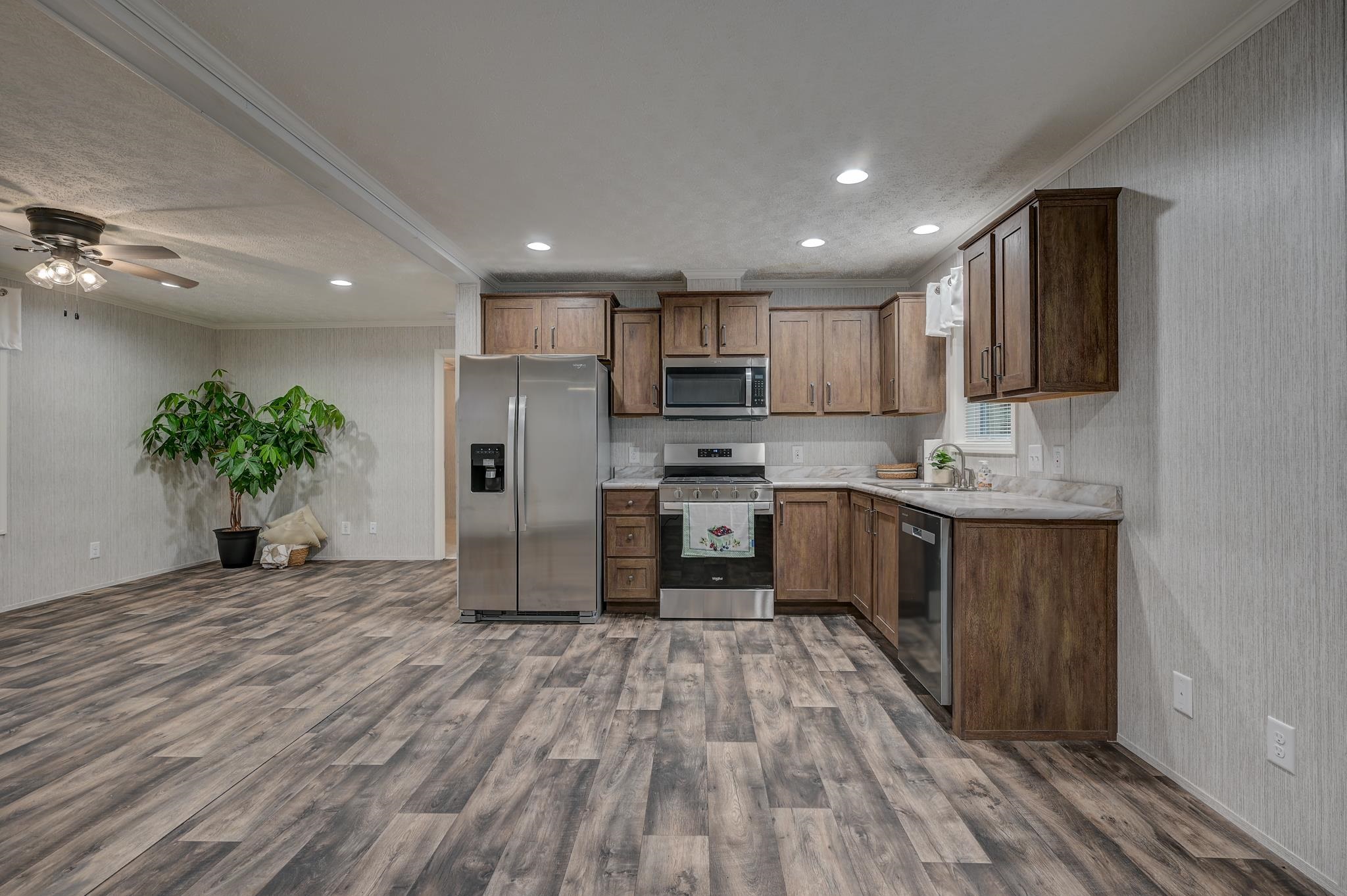 Kitchen with dark wood cabinets and stainless steel appliances, opening onto a spacious area with gray wood-look flooring.