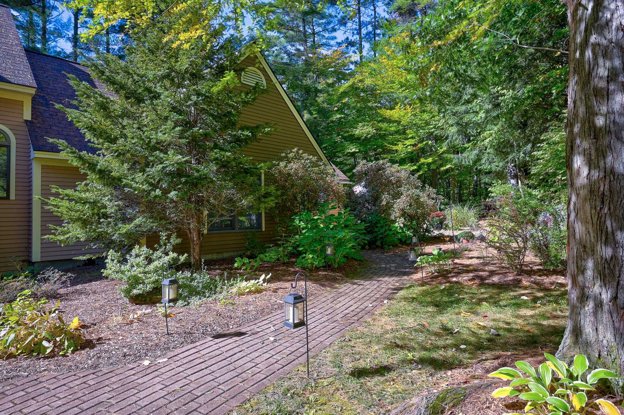 Brown-sided home framed by trees, with a brick walkway winding through the landscaped garden.