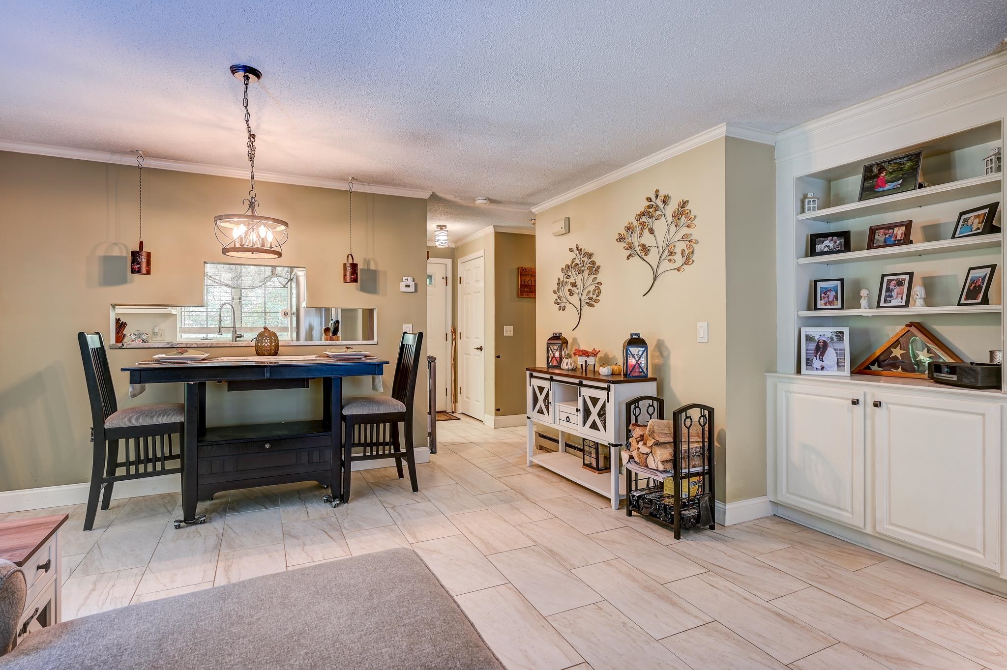 Dining area with a dark table, tiled floor, kitchen pass-through, and built-in display shelves.